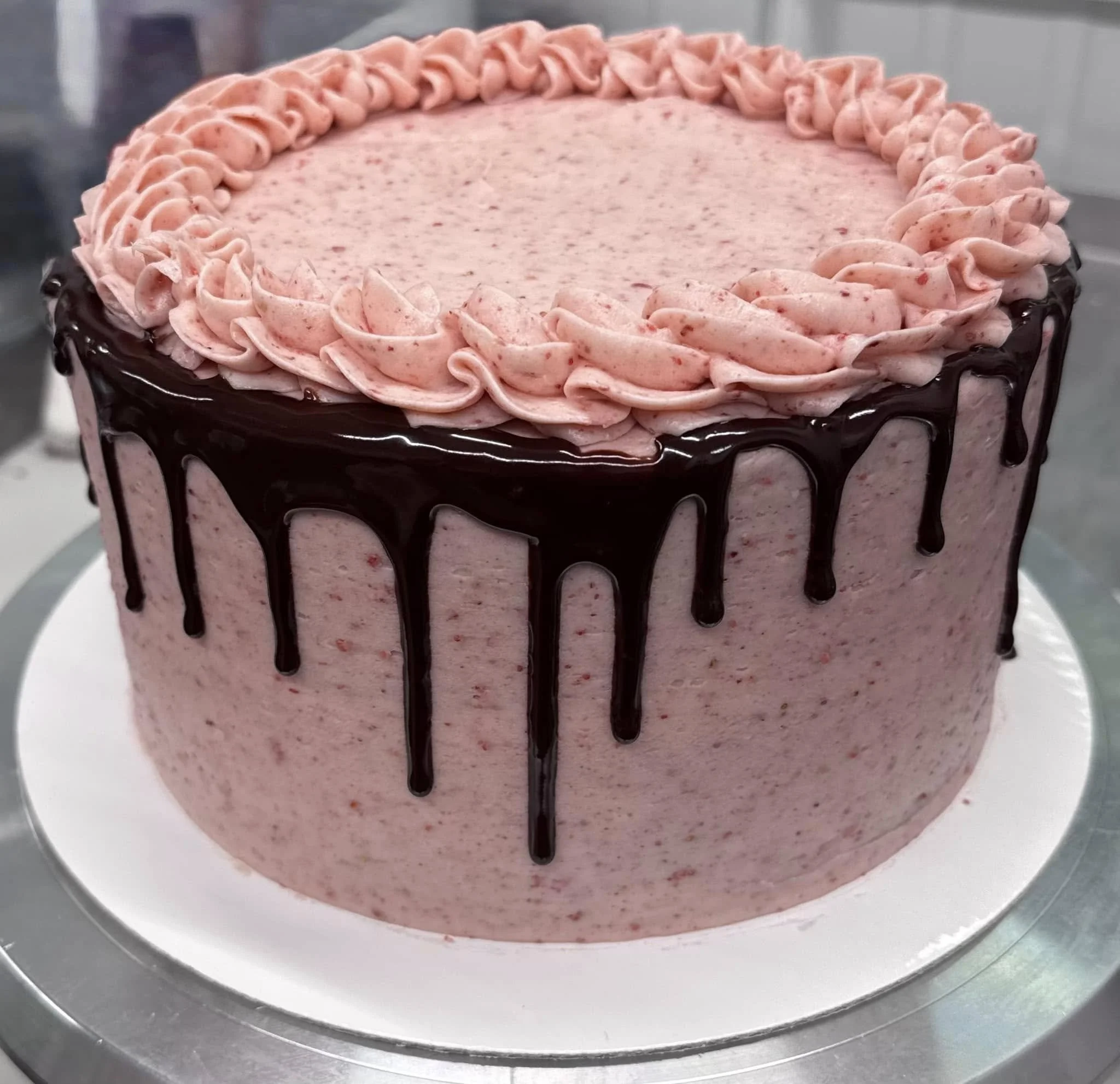 Pink ice cream with strawberry flecks, topped with pink whipped cream rosettes and drizzled with chocolate sauce, served on a white plate.
