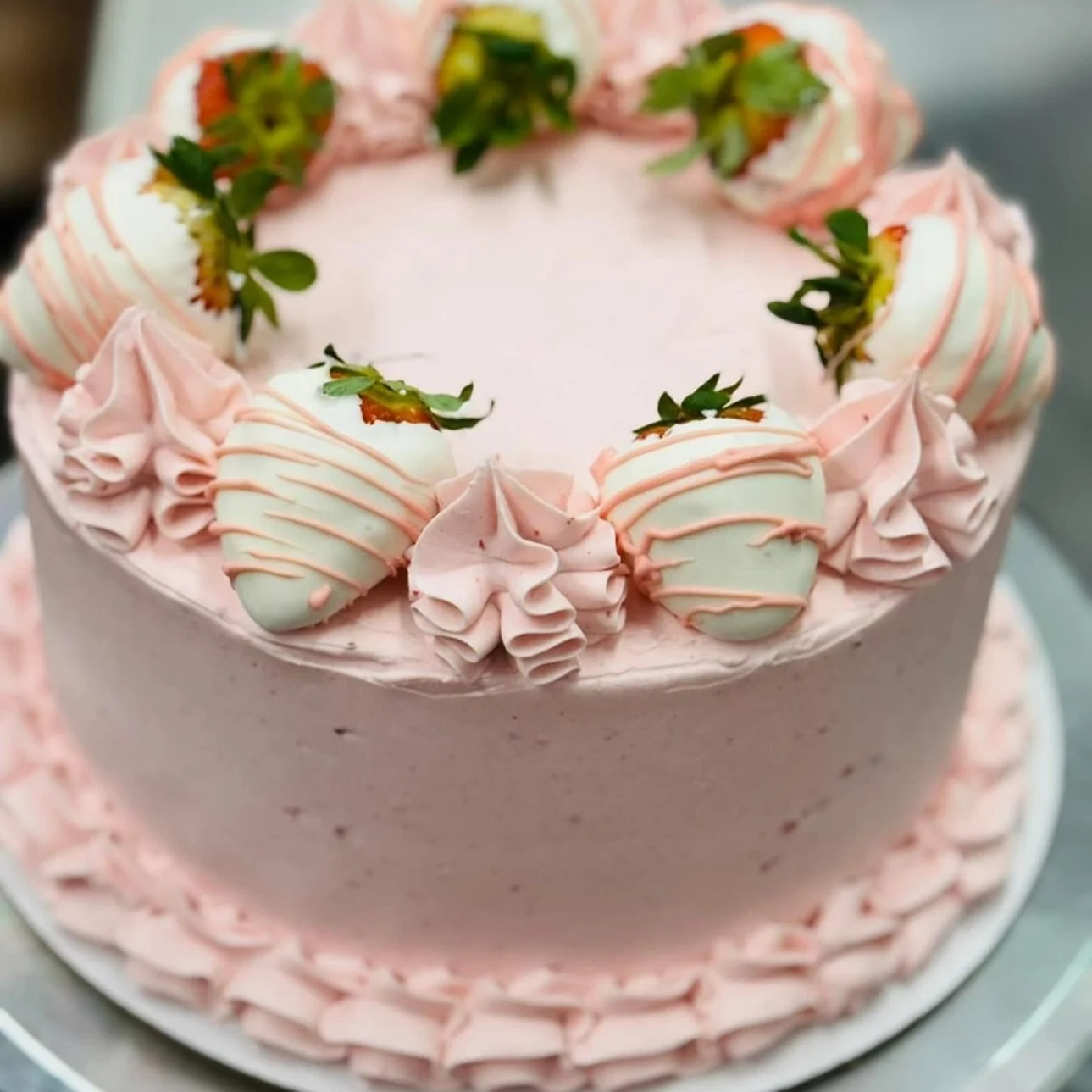 A pink frosted cake decorated with strawberries and pink drizzle, with piped pink frosting around the sides.