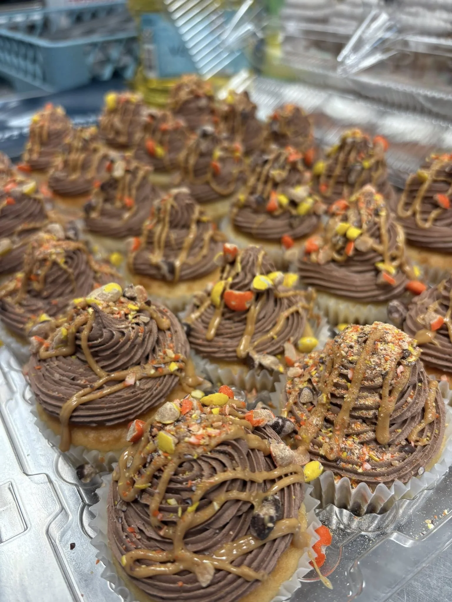 Close-up of cupcakes with chocolate frosting, colorful sprinkles, and caramel drizzle, arranged on a tray lined with paper cupcake liners.