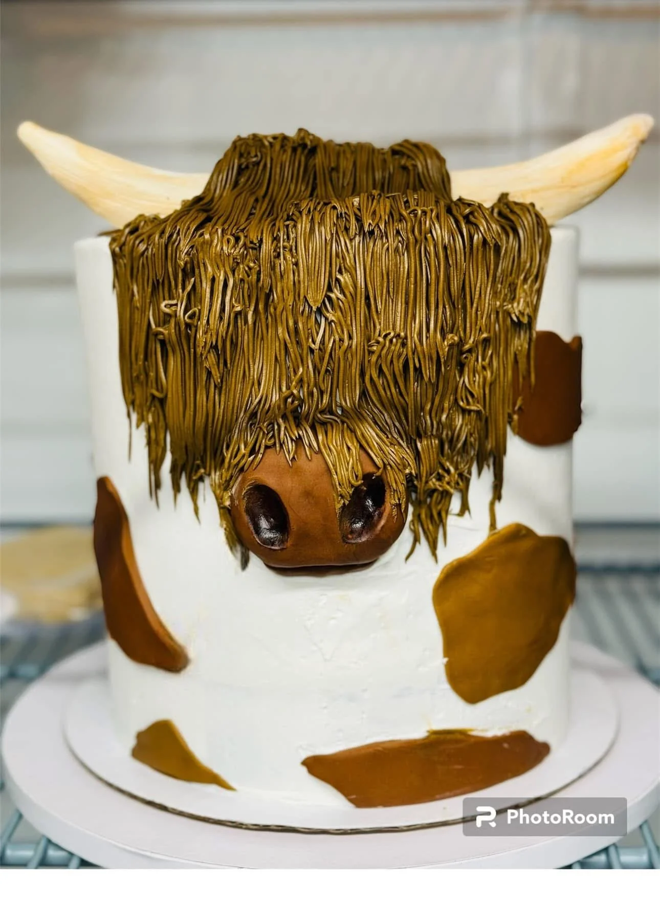 Cake decorated as a cow with white icing, brown spots, a cow's face with a snout, and a mane made of pasta.