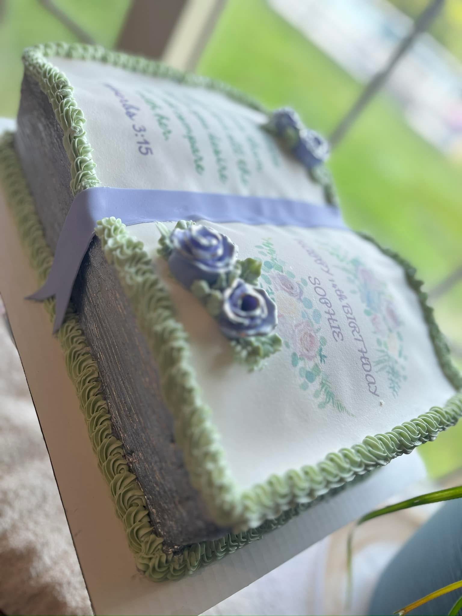 Decorative rectangular cake with white icing, green piped border, and blue floral decoration on top, placed on a white surface.
