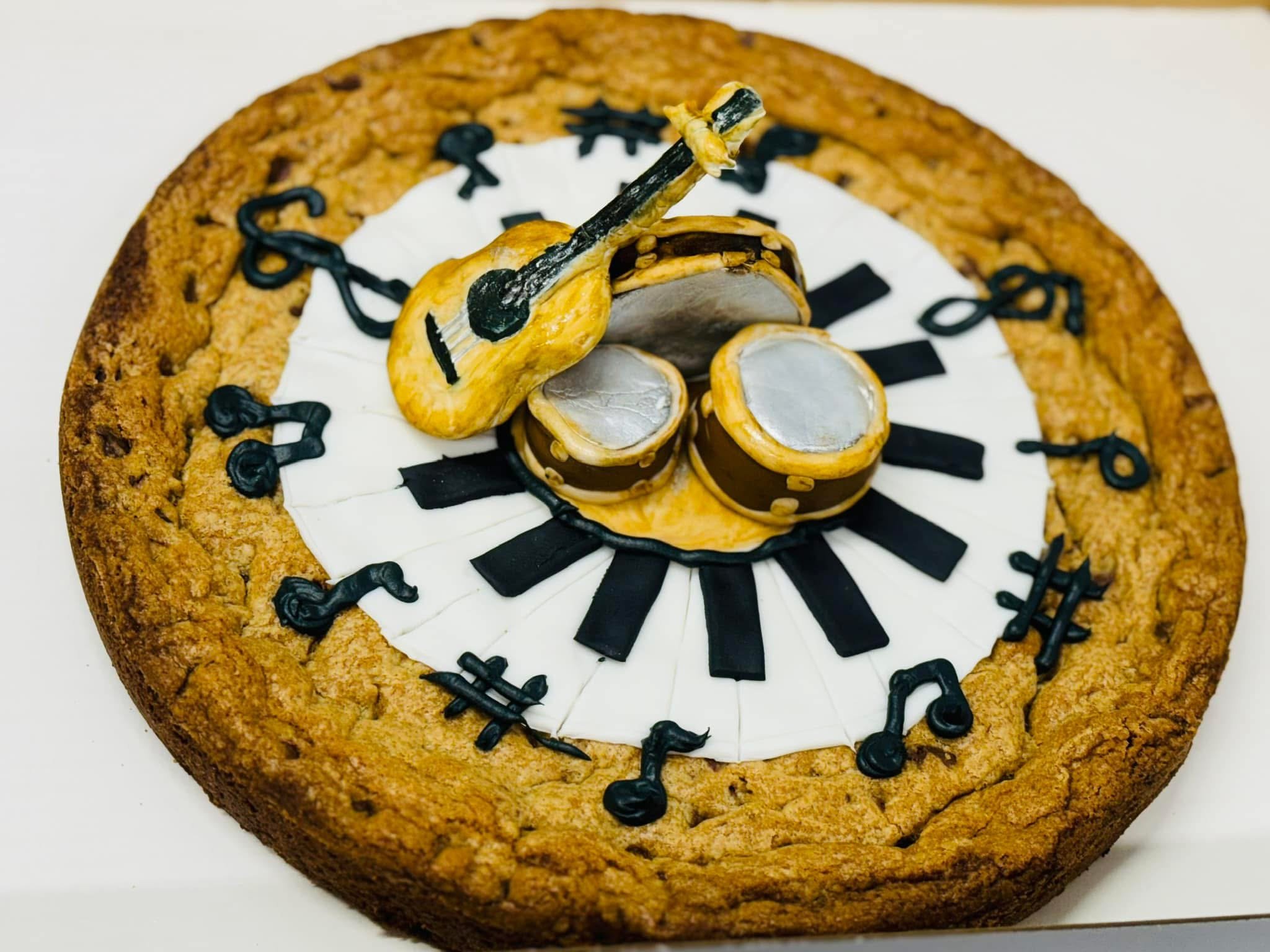Cookie cake decorated with musical notes, black and beige figurine of a girl holding a guitar, and black musical notes around the edges.