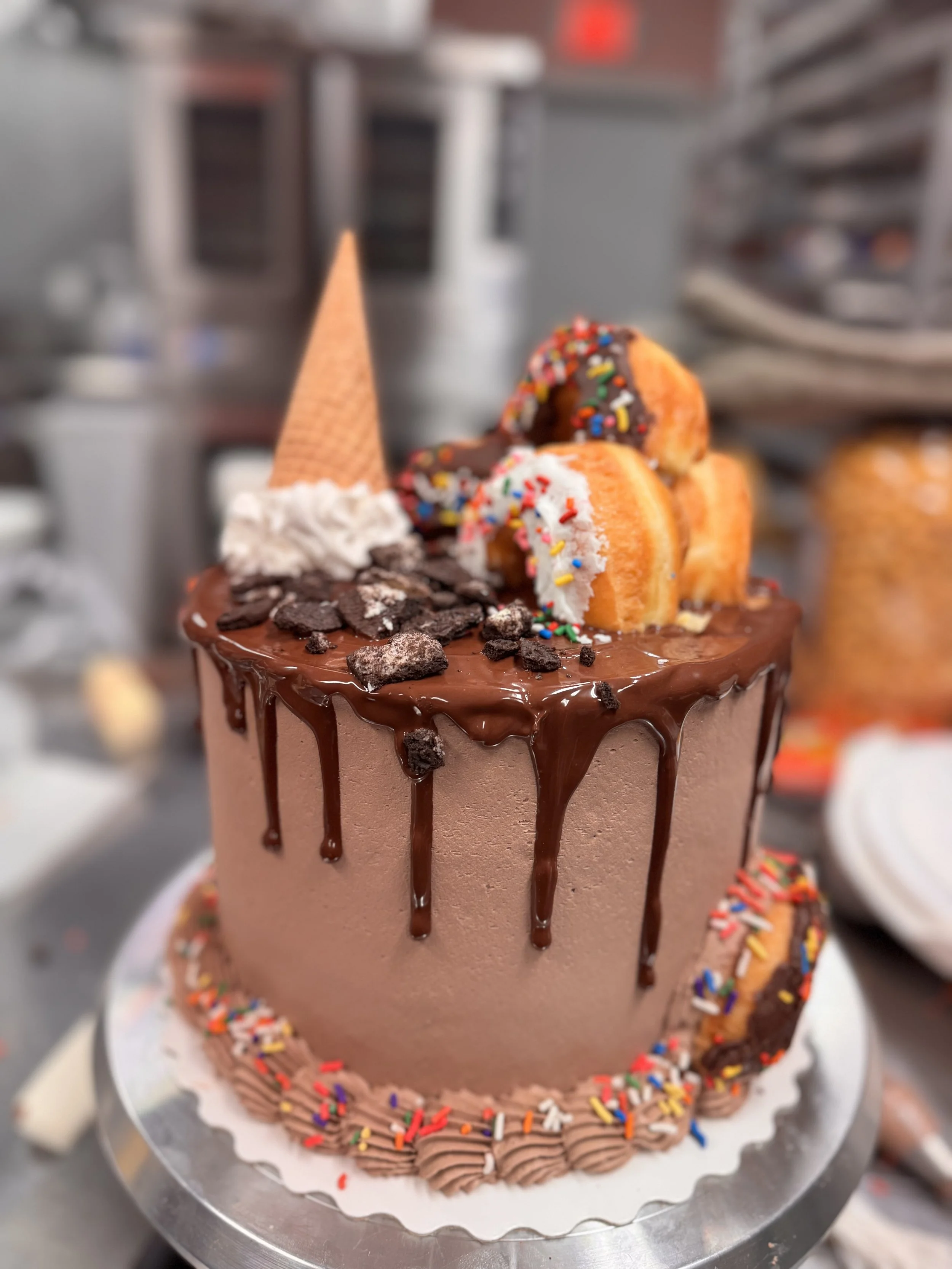 A chocolate cake with dripping chocolate ganache, topped with a cone, whipped cream, chocolate pieces, and bananas decorated with colorful sprinkles.