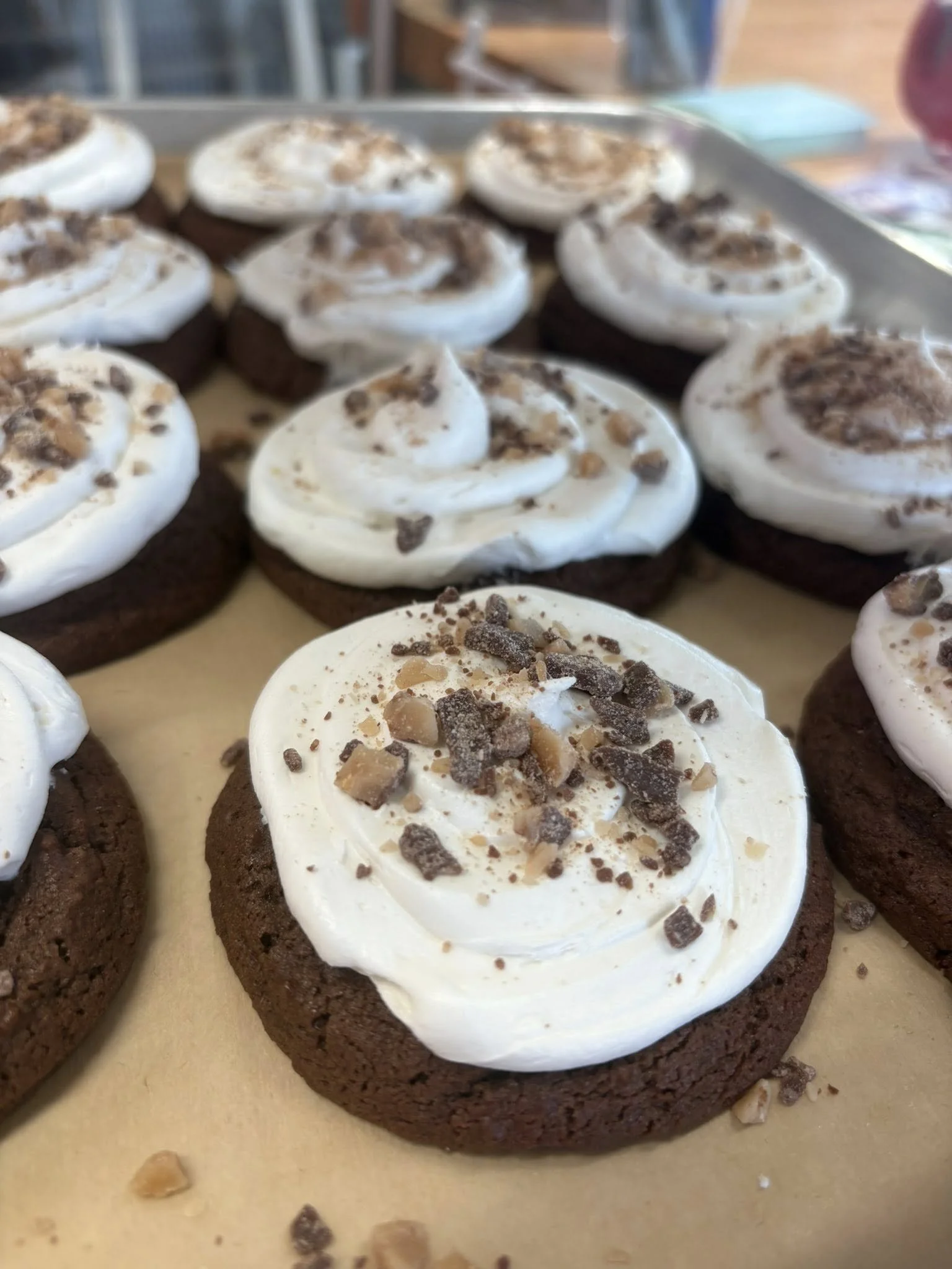 Close-up of several chocolate cookies topped with white frosting and sprinkled with chopped nuts.