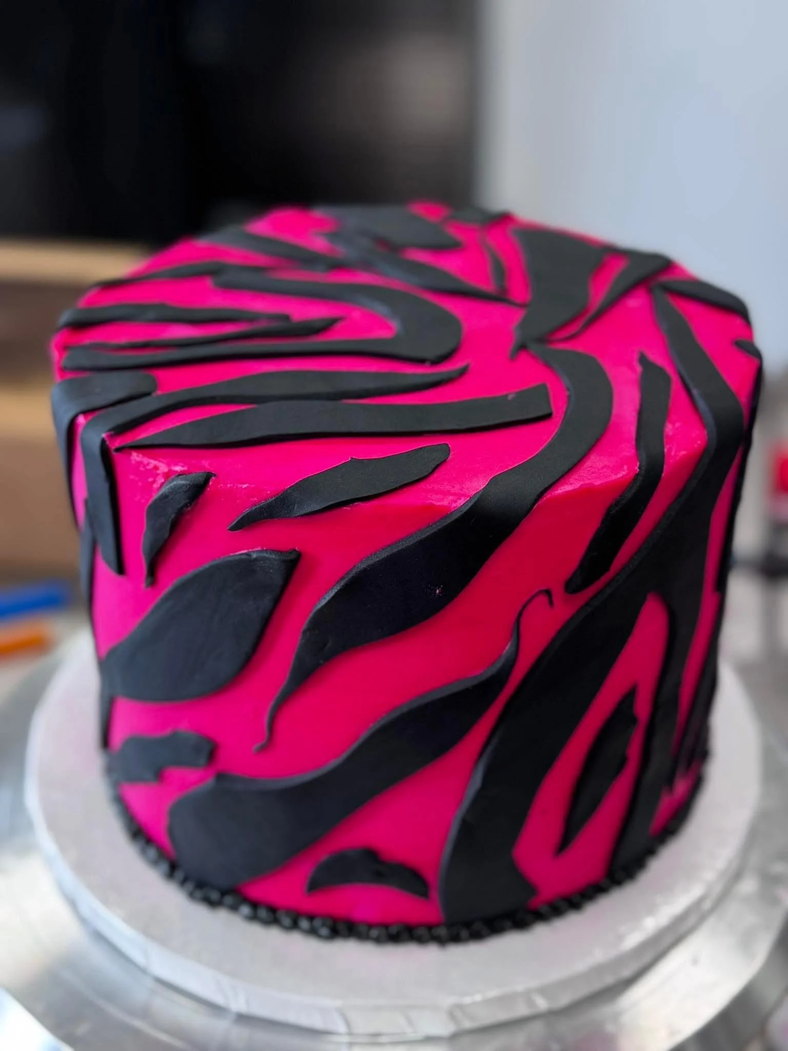 A colorful birthday cake with pink and black icing, decorated with black chocolate shapes resembling zebra stripes, on a silver platter.