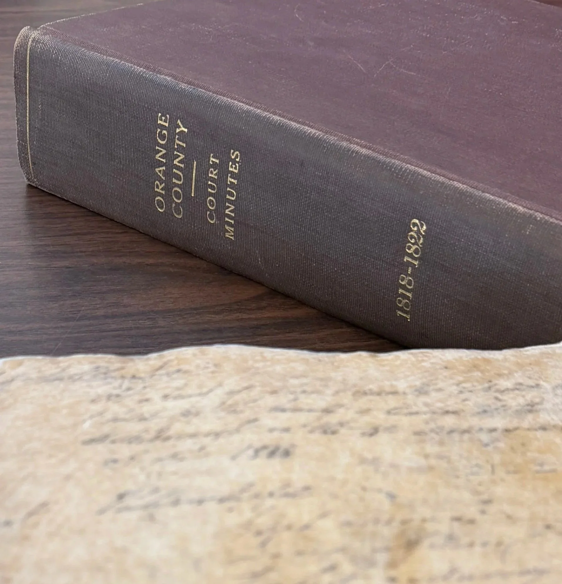 An aged document sitting next to a thick book spine reaading "Orange County Court Minutes, 1818-1822"  – genealogy research. © Butterworth Research