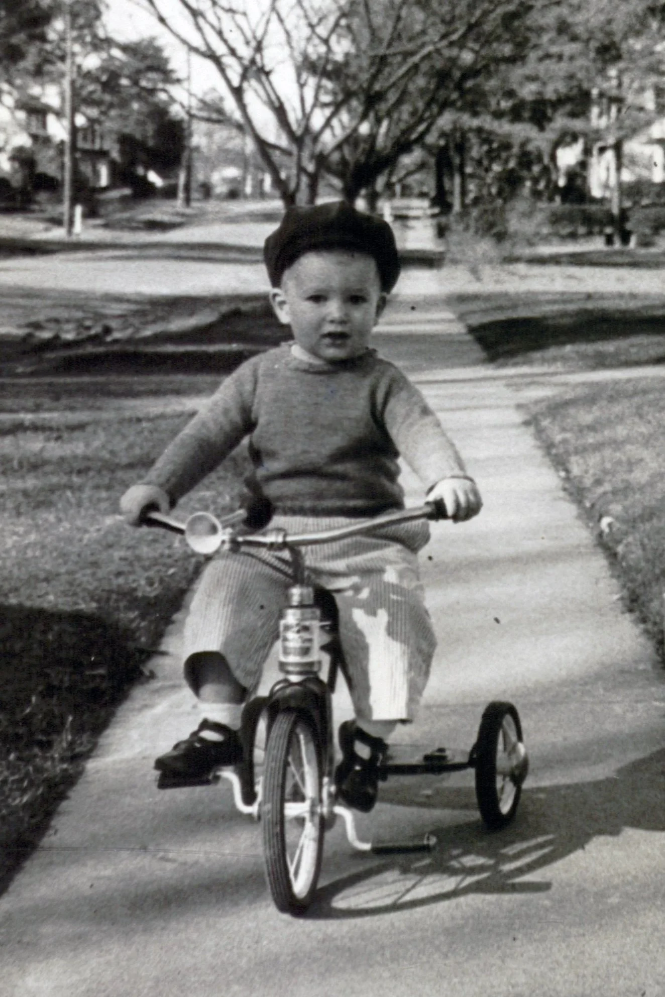A black and white photo of a very young boy in a sweater and cap rides a tricycle  – genealogy research. © Butterworth Research