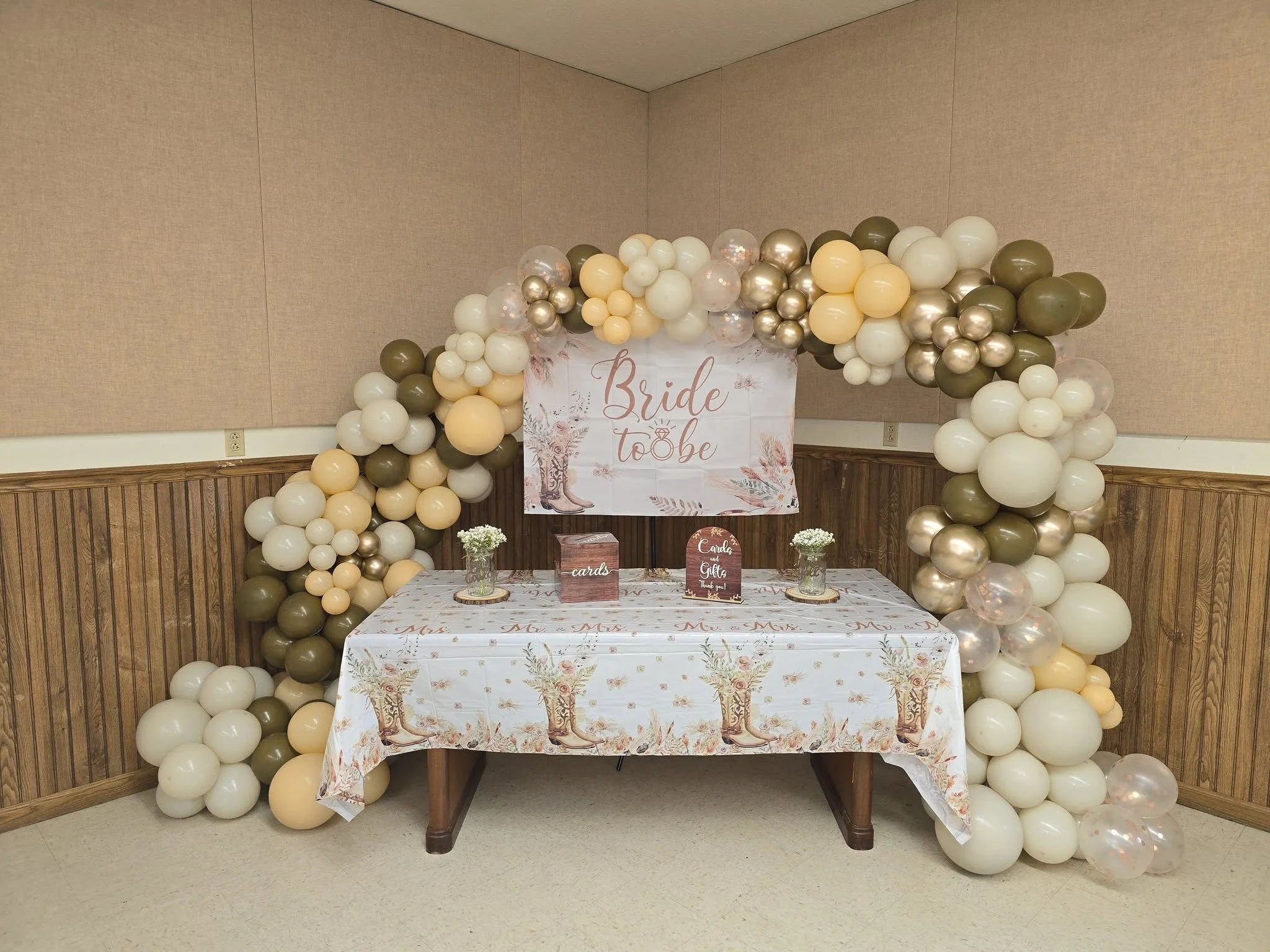 Decorative balloon arch with a 'Bride to Be' sign and a table with cards and gifts for a bridal shower.
