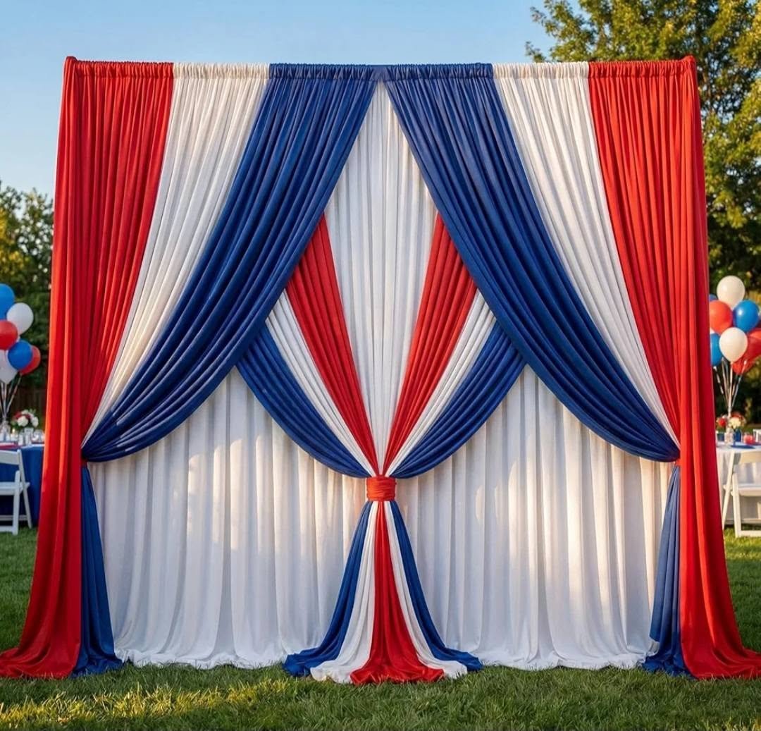 A patriotic red, white, and blue fabric backdrop with draped curtains tied in the center, set up outdoors with tables and balloons in the background for a celebration.