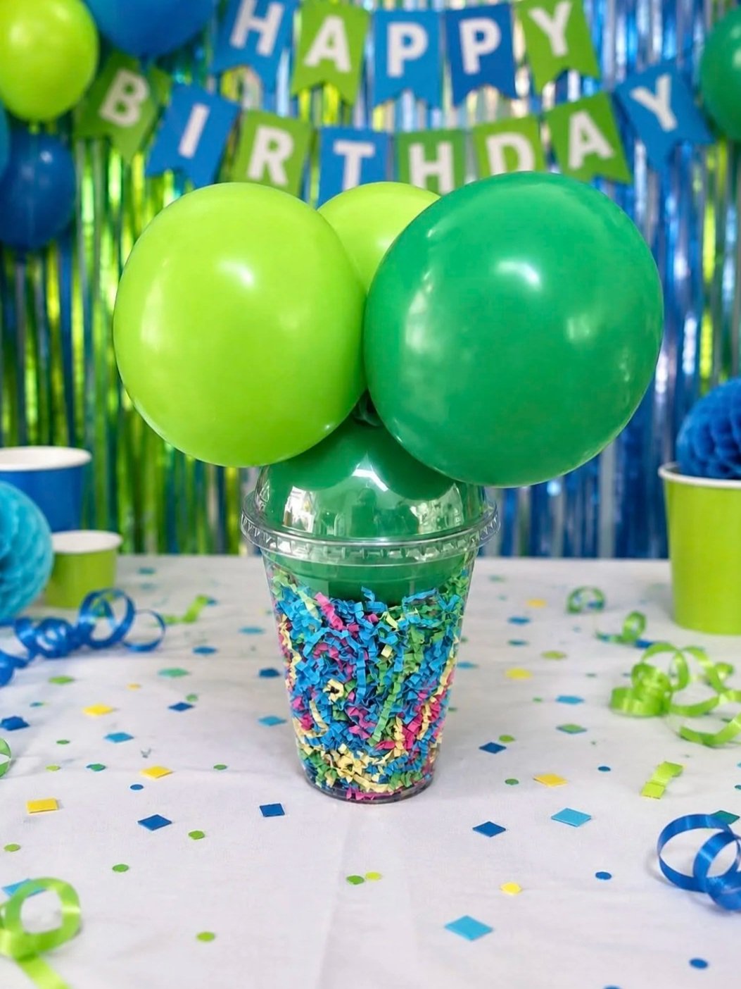 Colorful birthday party decorations with green and blue balloons, confetti, and a banner that says "Happy Birthday" in the background.