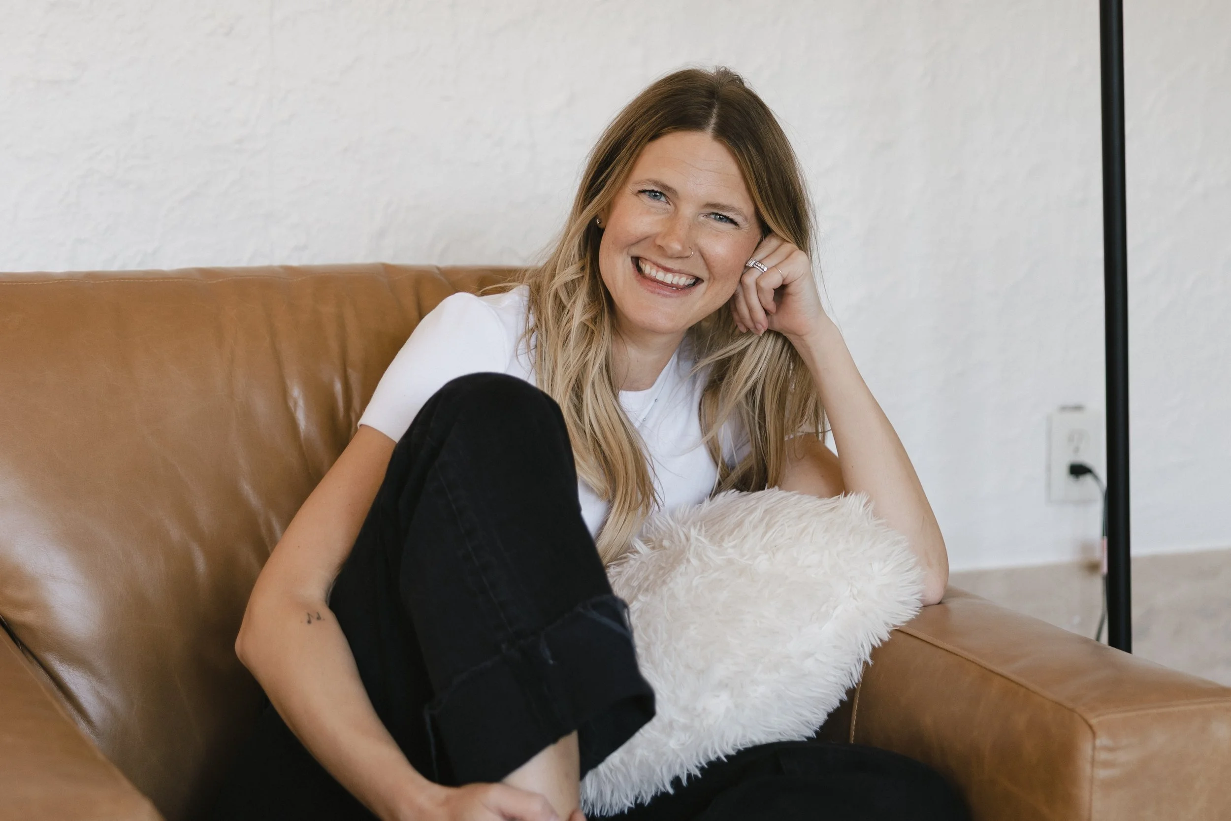 Therapist Chanelle Johnson smiling while seated on a brown leather couch.