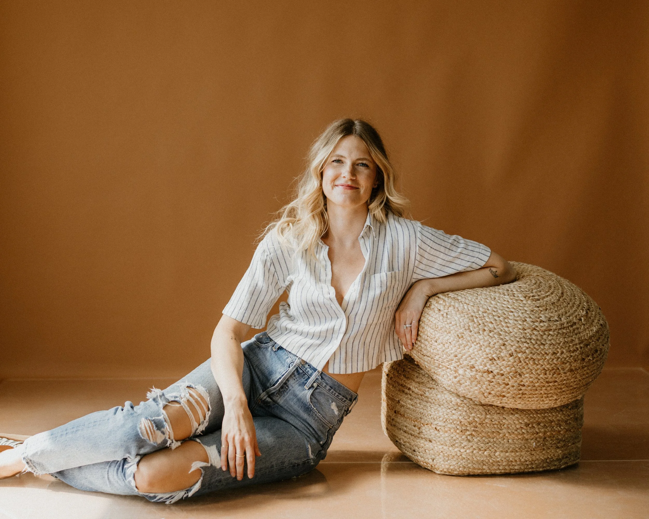 Chanelle Johnson seated beside a woven pouf against a warm brown backdrop.