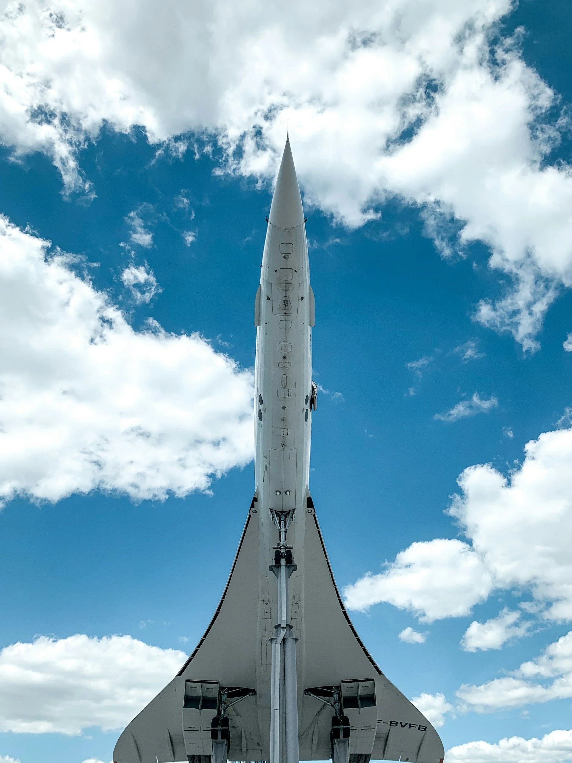 View of the underside of an airplane tail and fuselage against a partly cloudy sky.