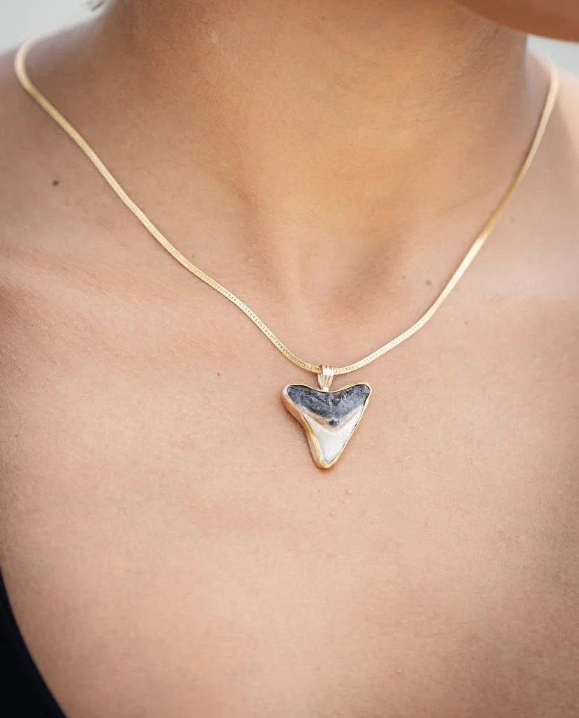 Close-up of a person's neck and upper chest wearing a gold necklace with a large, irregularly shaped black and white pendant.