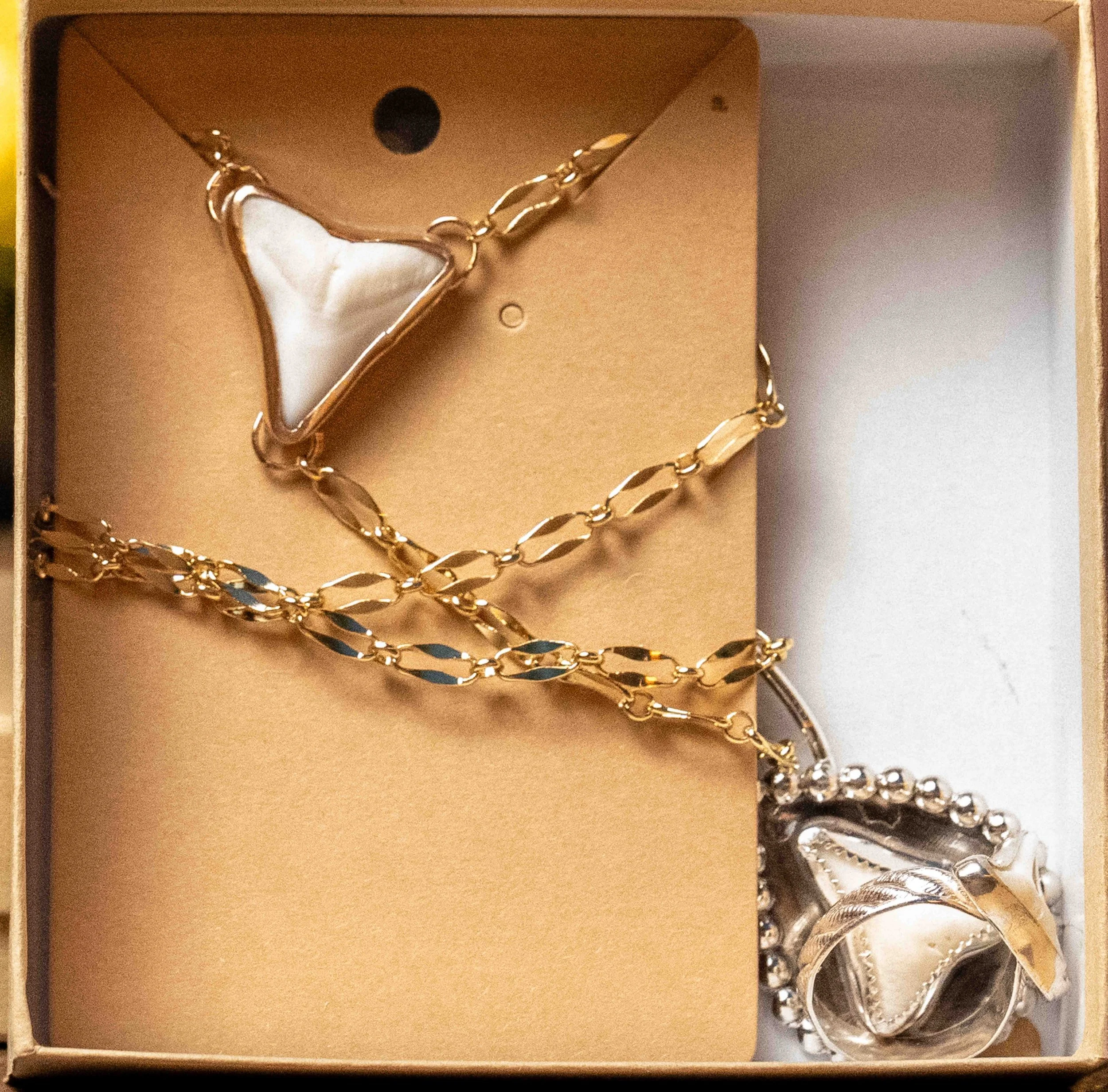 Gold and silver jewelry, including necklaces and rings, arranged in a jewelry box with a beige background.