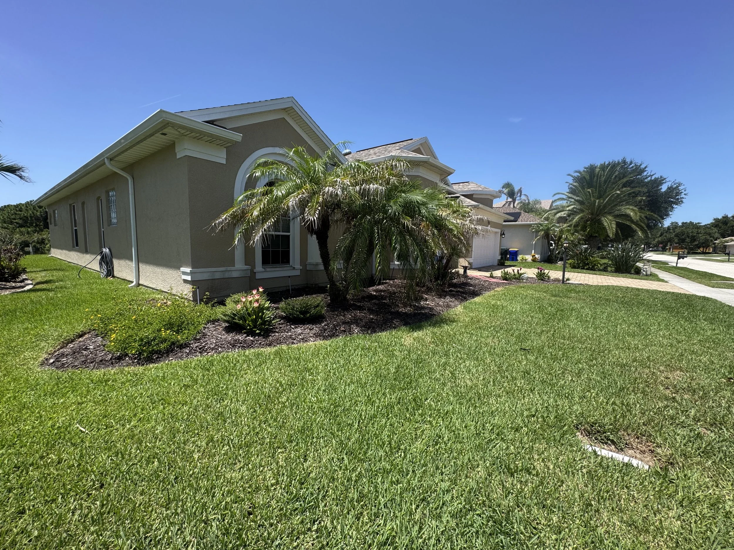 A suburban house with a well-maintained lawn, palm trees, and a blue sky.