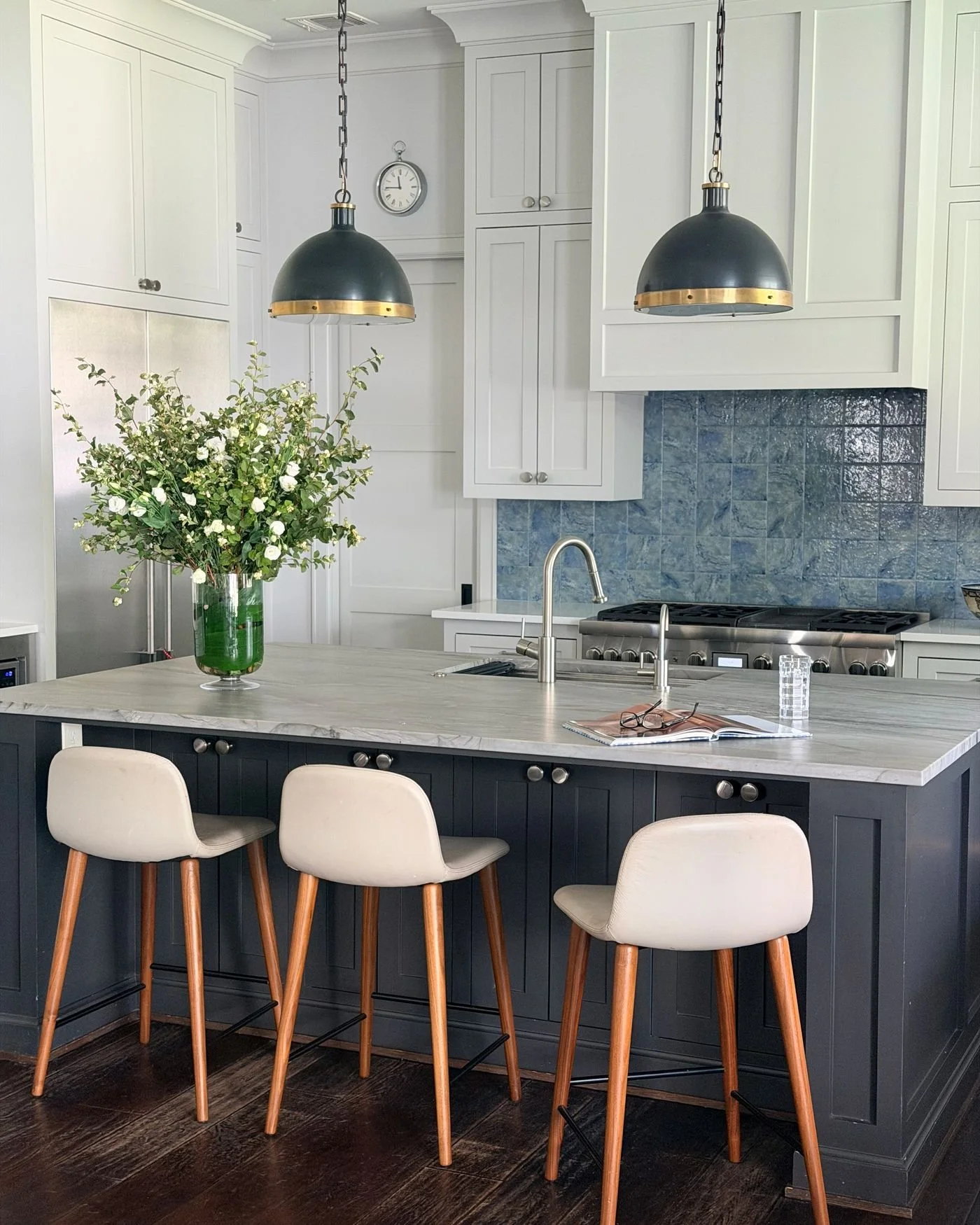 Kitchen with a navy island, brass pendants and white counter stools