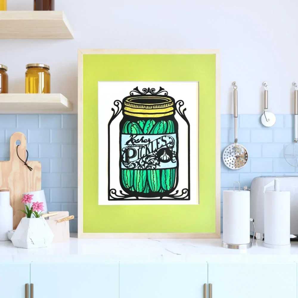 Whimsical papercut pickle jar with colorful tissue paper inlay framed and displayed in bright kitchen
