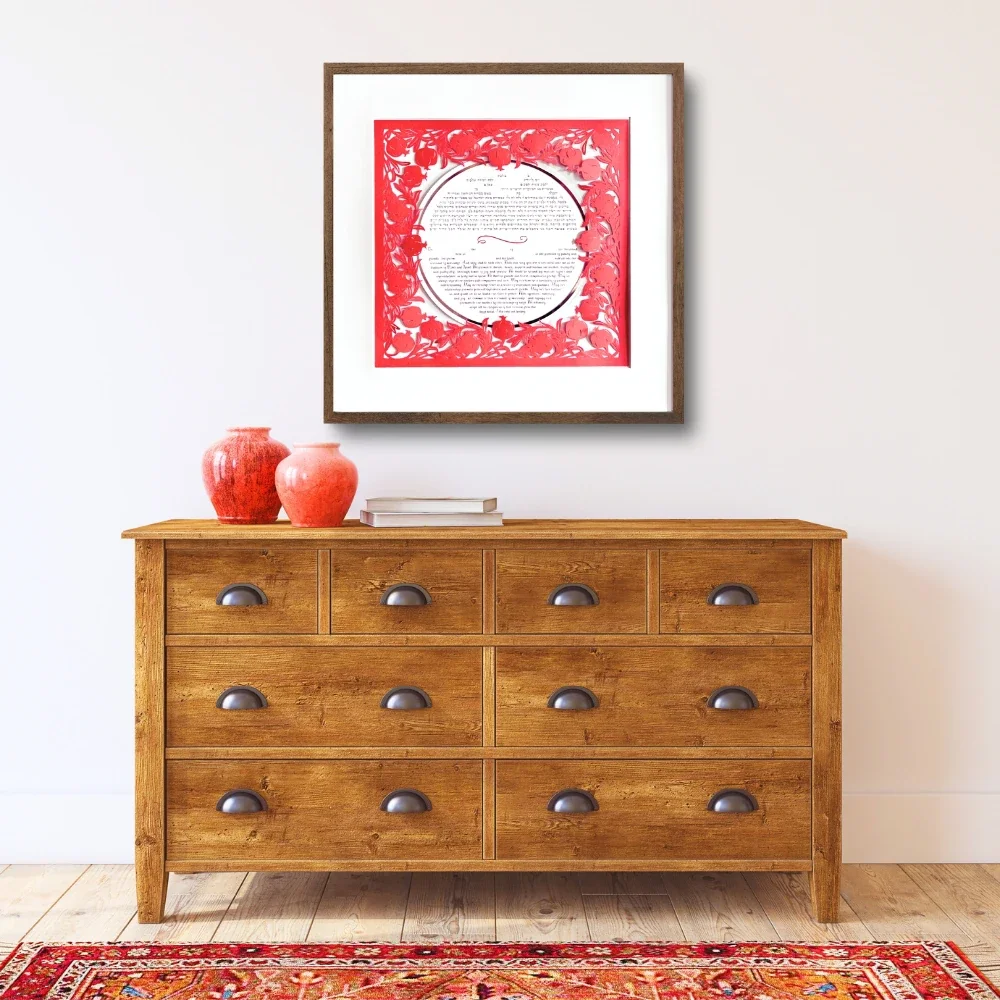 Red pomegranate papercut ketubah in black frame hanging on a bedroom wall