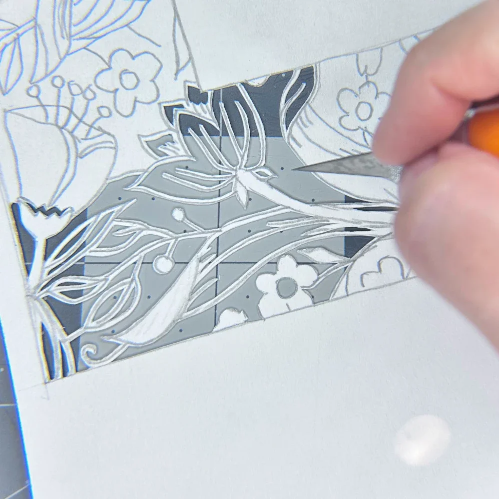 A close-up of a hand using a craft knife to carve intricate floral designs on paper, showcasing detailed artistry and creativity.