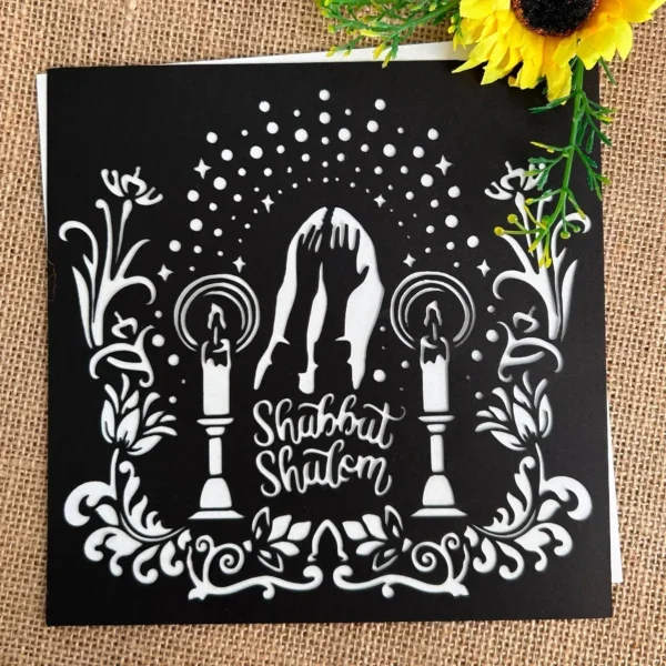 Shabbat papercut Judaica art with candles and challah, Jewish home blessing decoration. Laid out on fabric with a flower