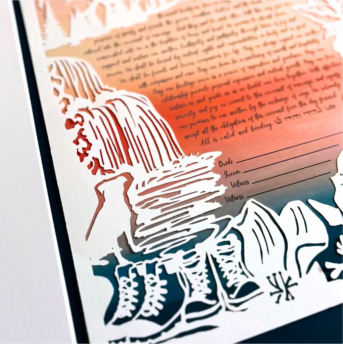 A close up of the paper-cut artwork ketubah, depicting a pair of boots, a dog, and a waterfall beside the handwritten marriage contract.