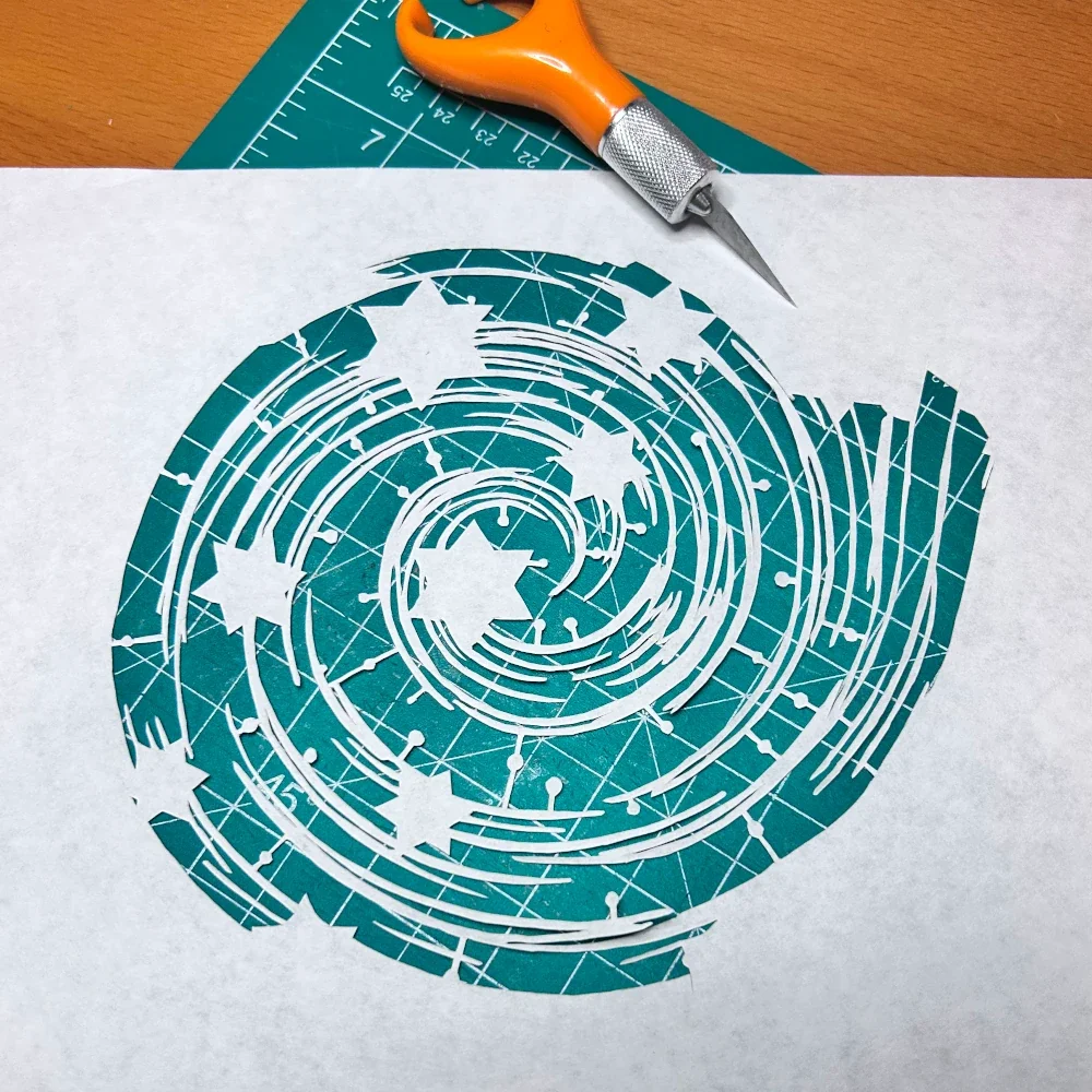 Intricate paper cut design featuring a spiral pattern with stars, showcasing creativity and craftsmanship on a cutting mat.