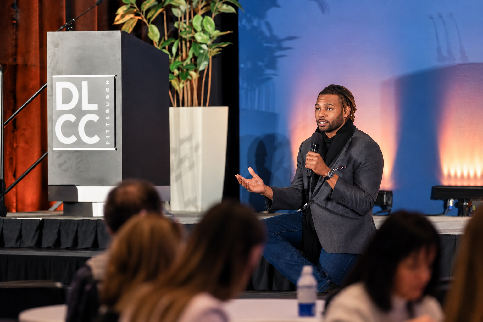 Keenan Medlock speaking to a live audience with a microphone onstage.
