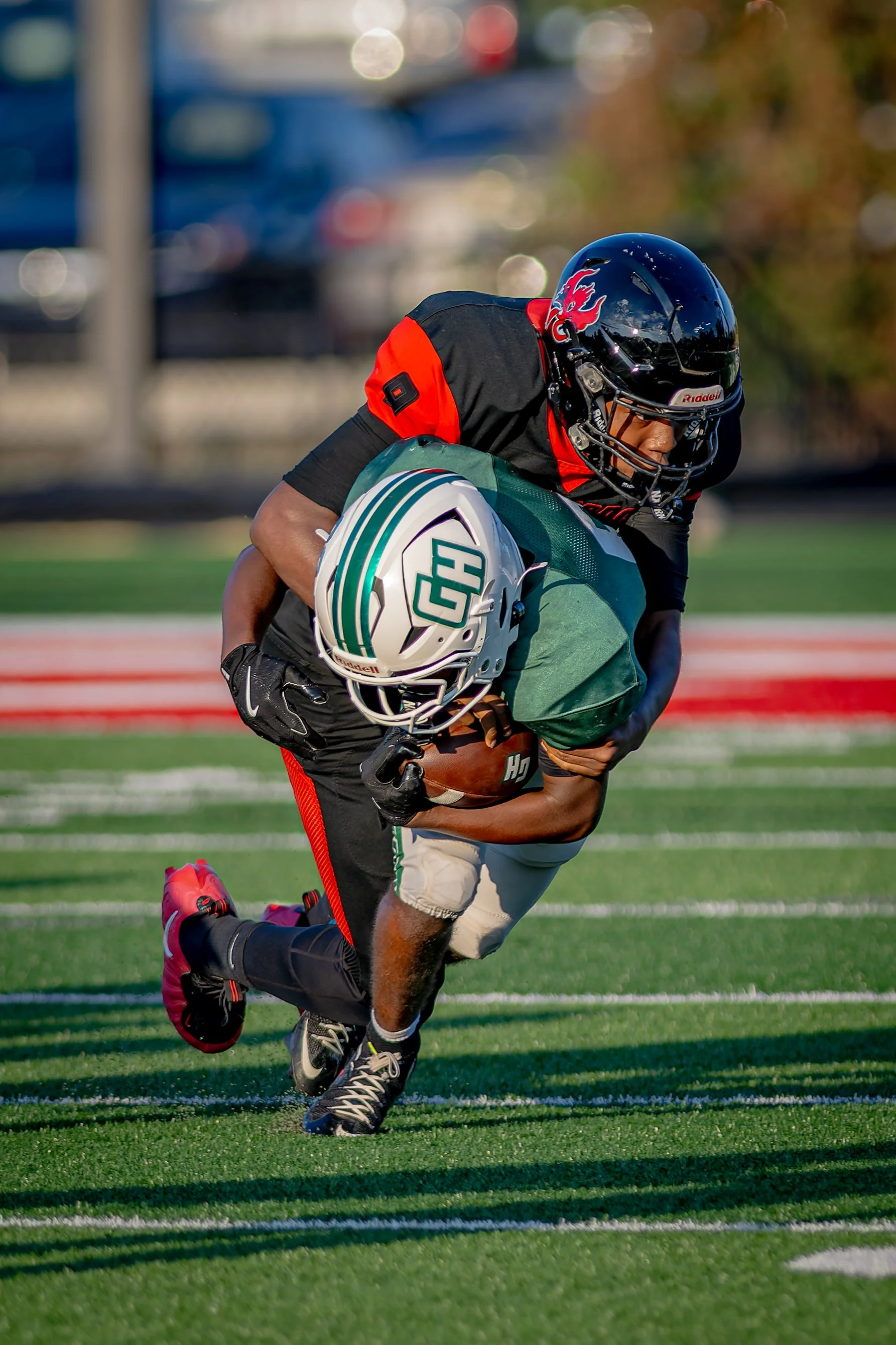 A football player in black and red uniform running with the ball on a green field, wearing a black helmet with a red dragon emblem.