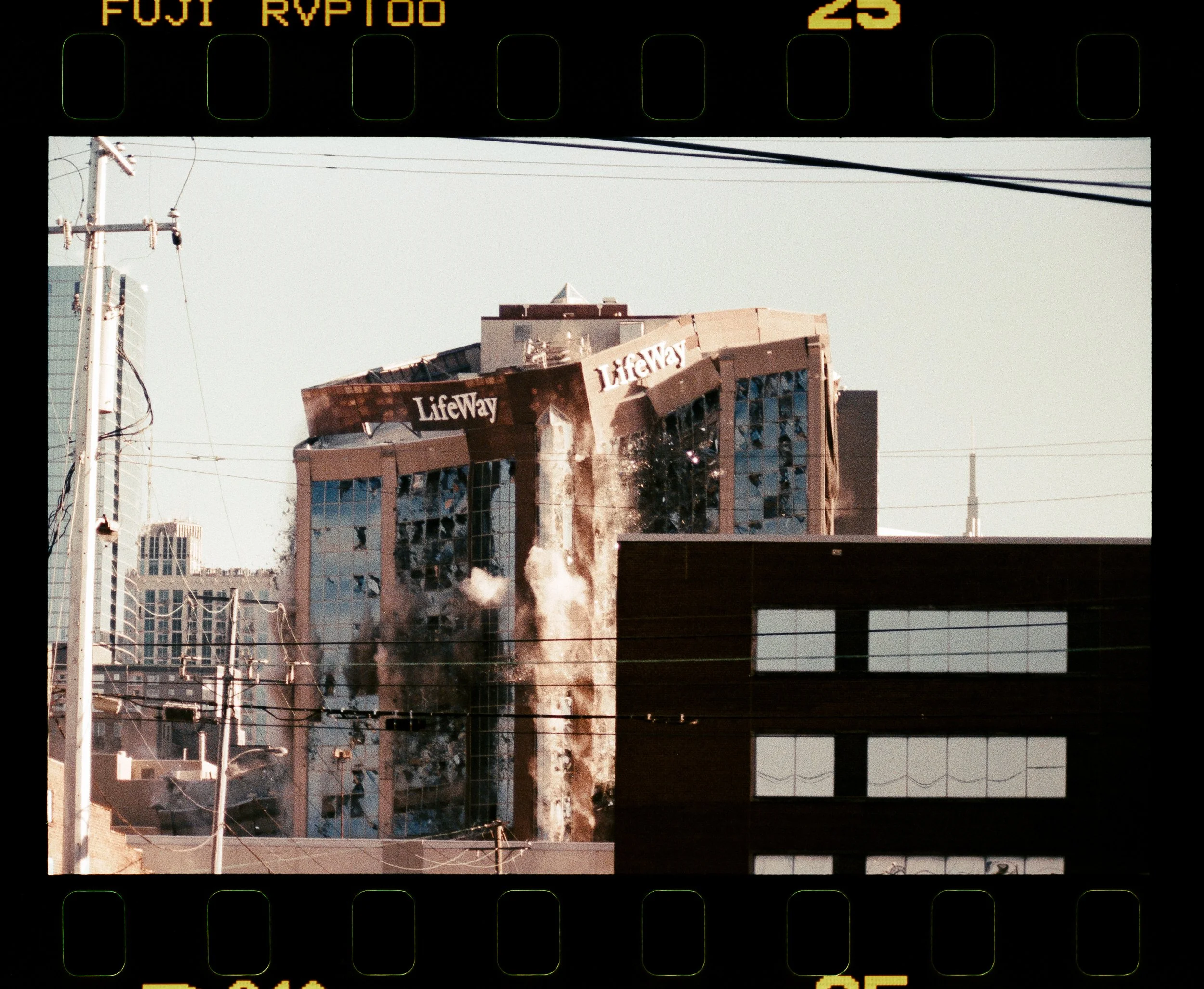 A cityscape showing damaged buildings with the 'Lifeway' sign, utility poles, and wires, under a clear sky.