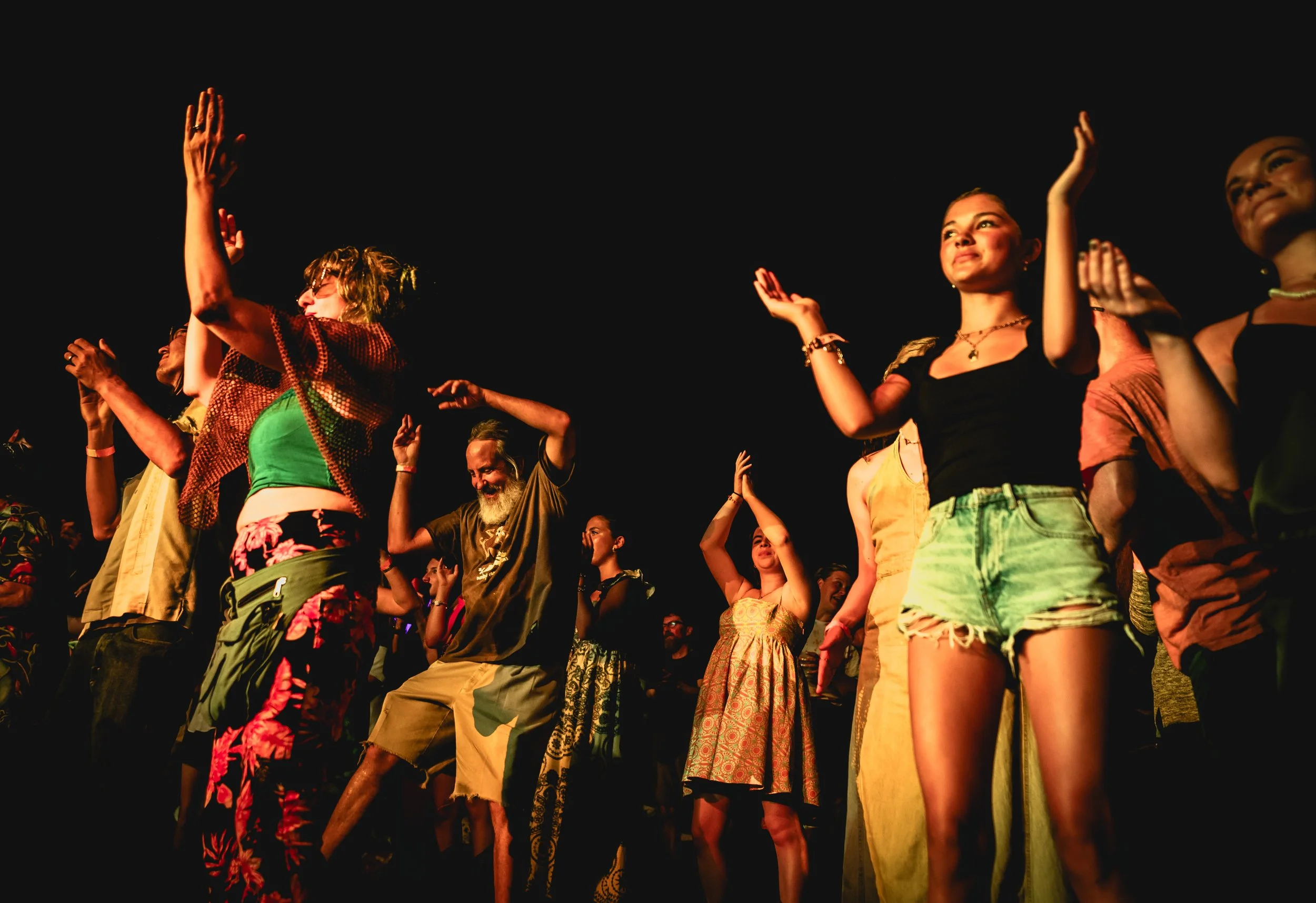 People dancing outdoors at night, raising their hands and enjoying the music.