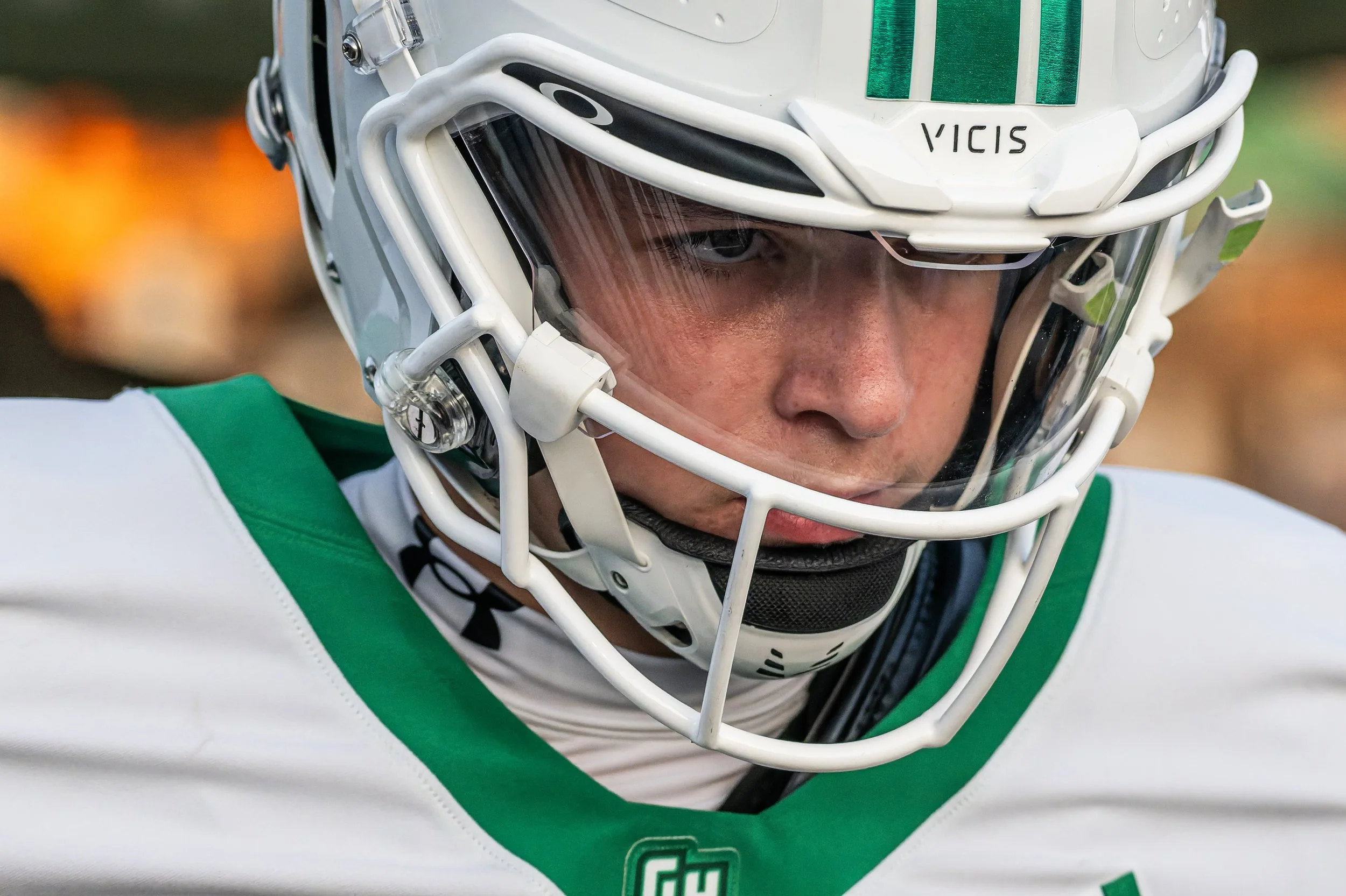 Close-up of a football player wearing a green and white uniform and a white helmet with a faceguard, focusing on the face through the helmet's face shield.