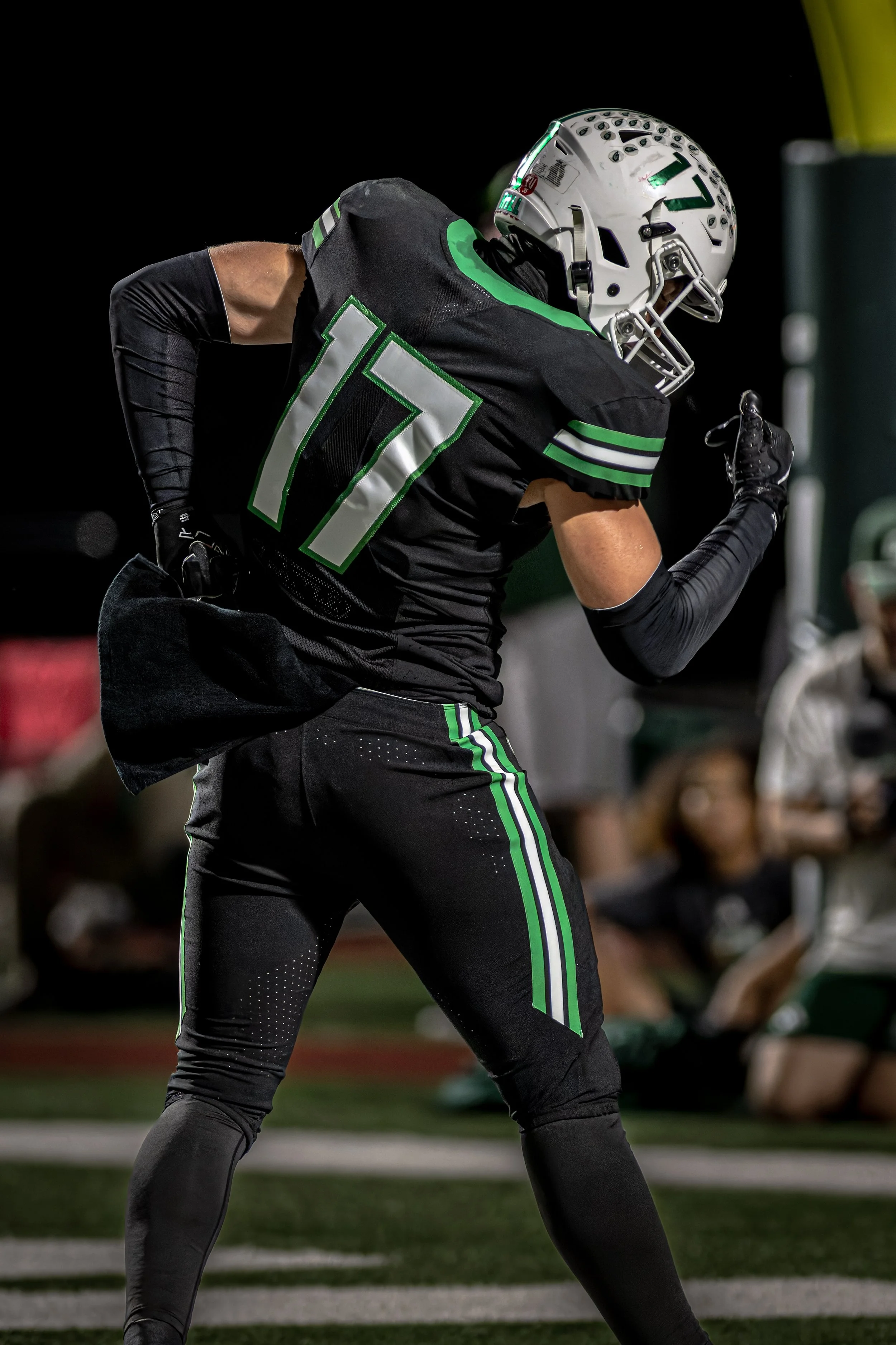 A football player in black and green uniform with the number 17 on the jersey, wearing a white helmet, running on the field during a game.