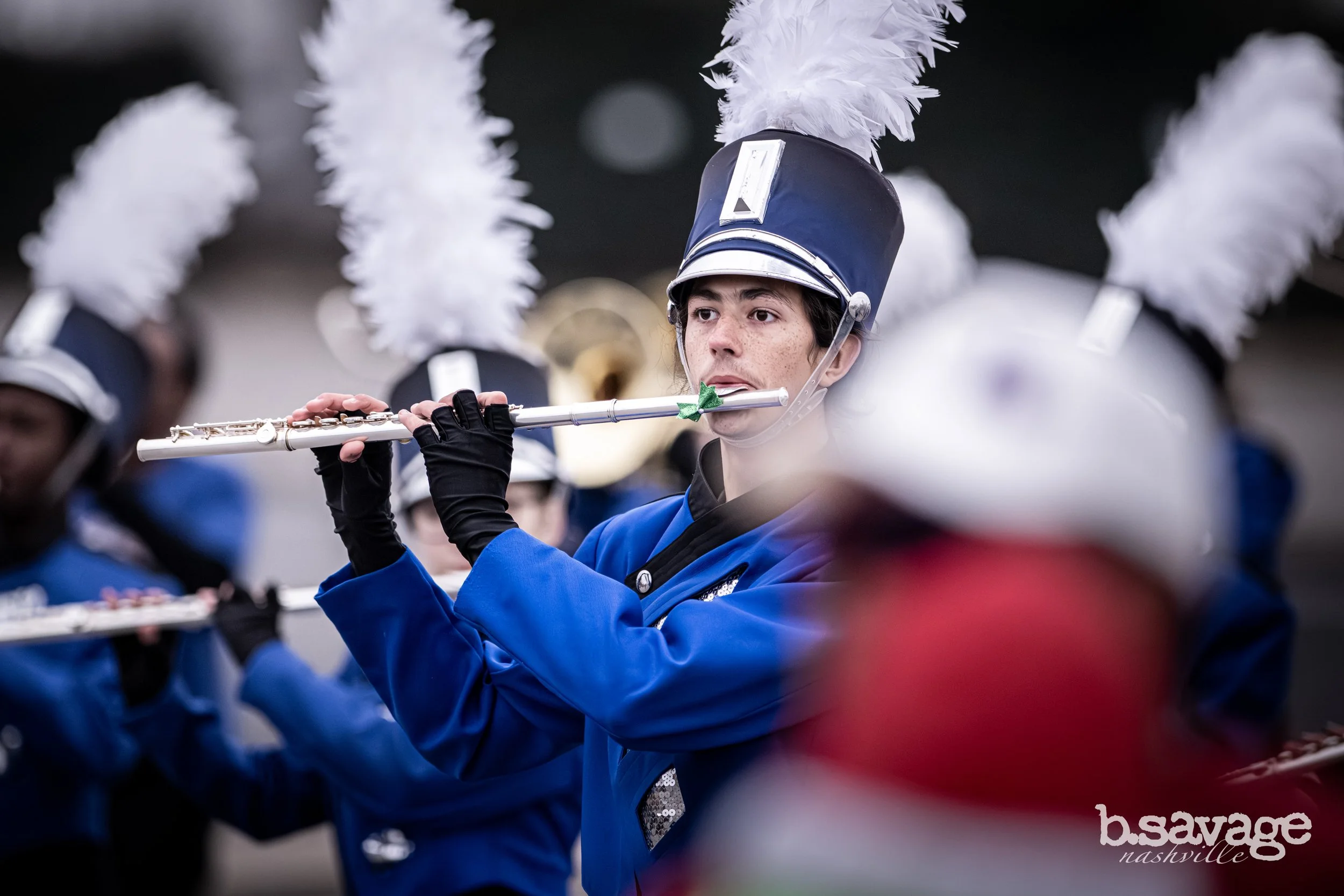 A young woman in a marching band uniform playing the flute during a parade.