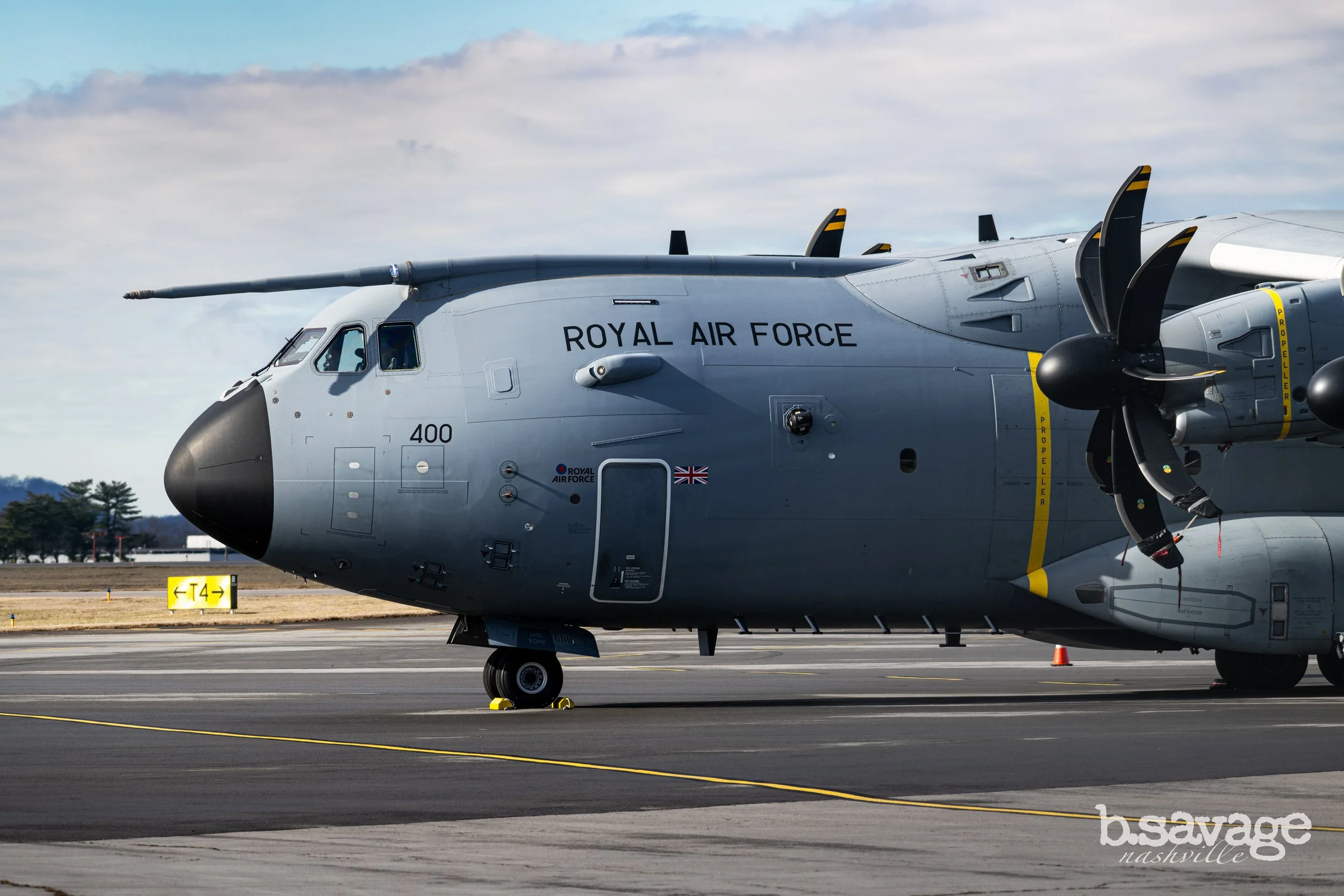 A military aircraft marked Royal Air Force parked on an airfield with clear sky and trees in the background.