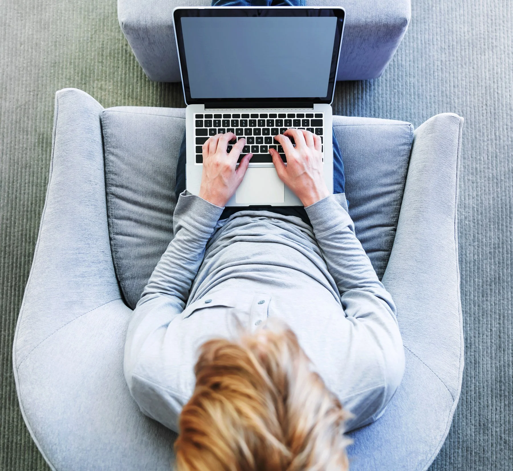 Overhead view of a person typing on a laptop in a grey armchair