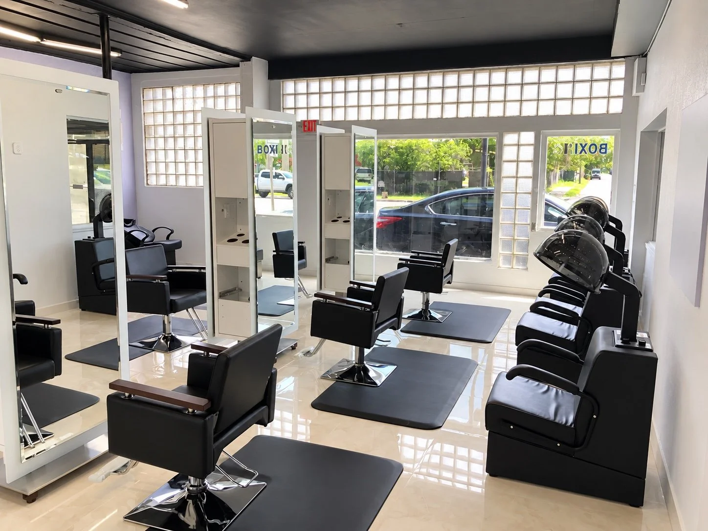 Salon interior with white mirrored styling stations, integrated storage, and black salon chairs.