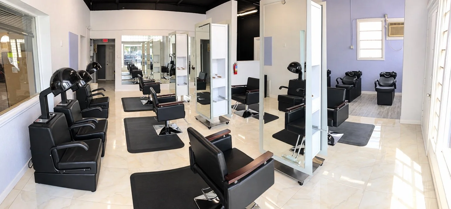 Wide view of the salon layout with mirrored styling stations, dryer seating, and shampoo area.