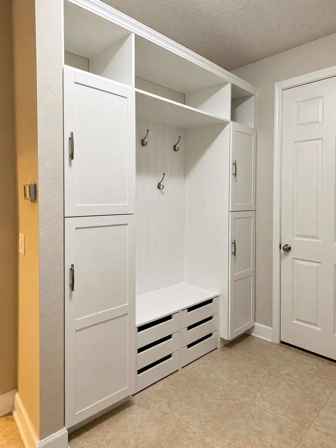 Angled view of custom white mudroom cabinetry, bench, and coat hooks.