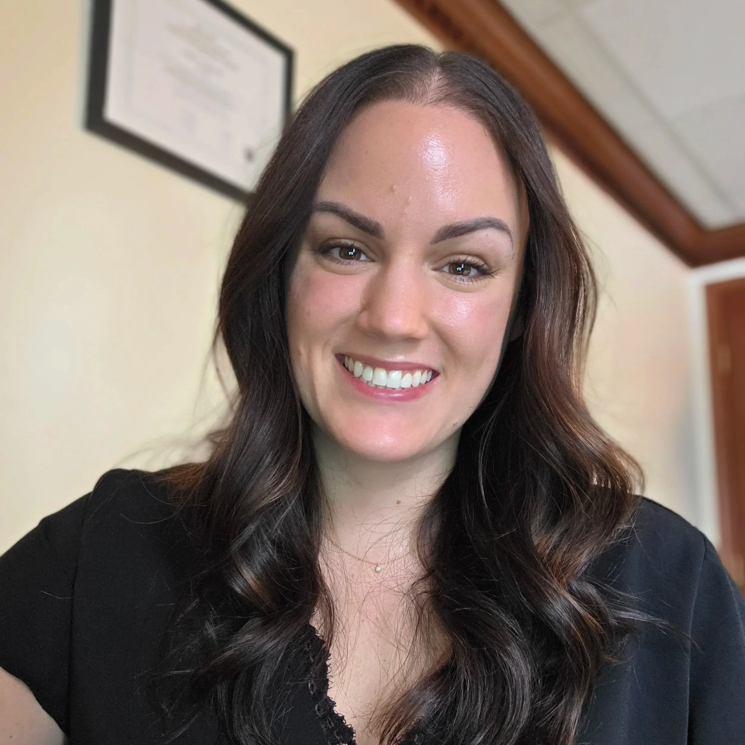 Close-up of a woman's face showing her forehead, eyes, eyebrows, smile, with long curled dark hair and wearing a black top.