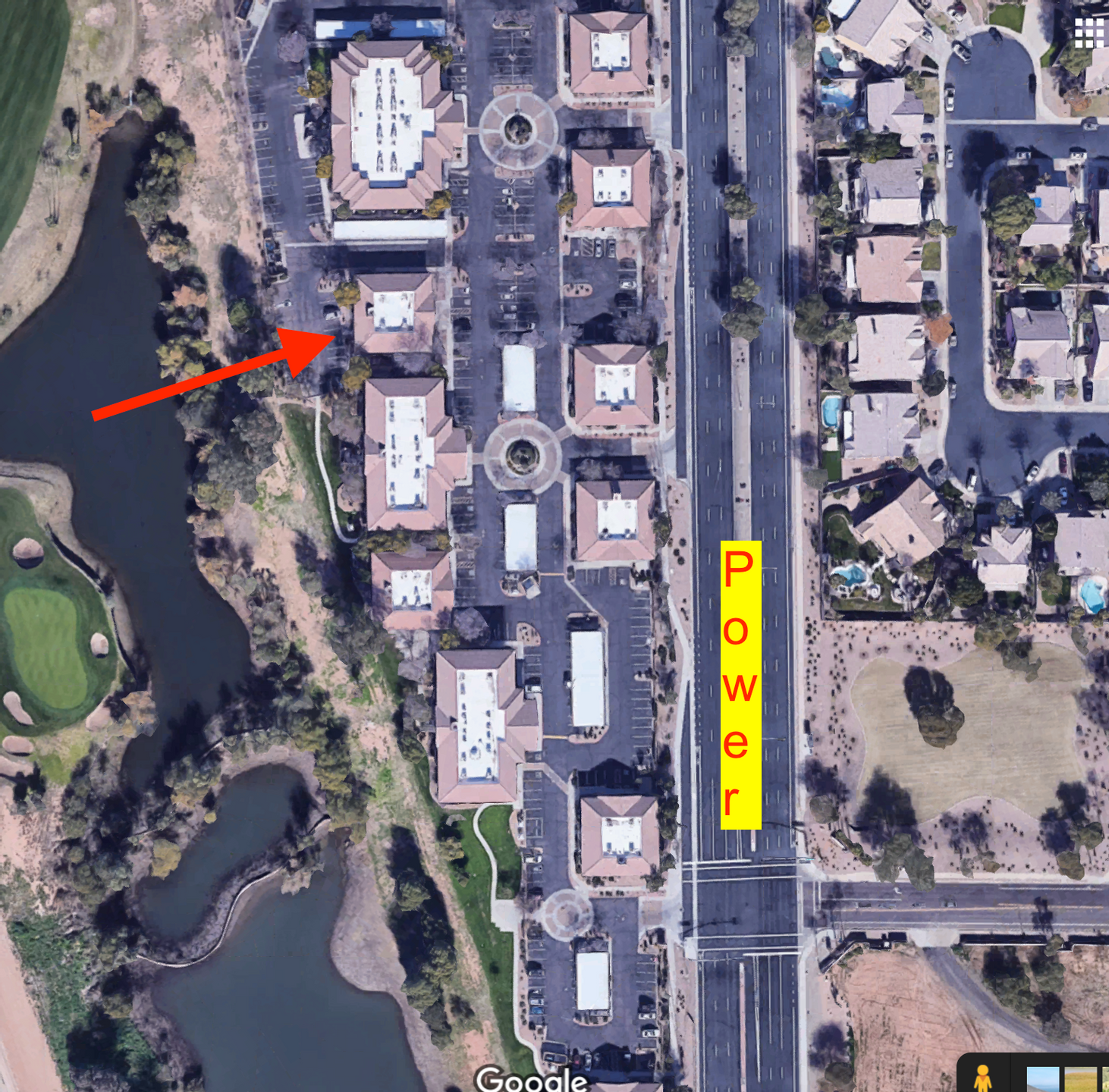 An aerial view of a parking lot area adjacent to a river or pond, with buildings and trees. A yellow label with red text reads "Power". An orange arrow points toward the river or pond on the left side of the image.