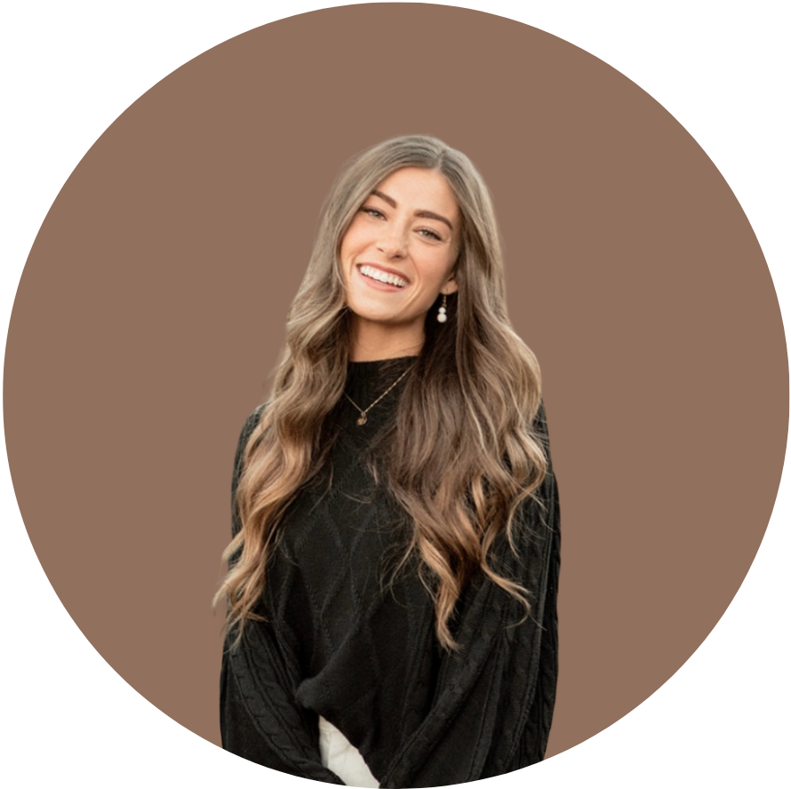 A young woman with long, wavy brown hair, smiling and winking, wearing a black sweater and pearl earrings, with a brown background.