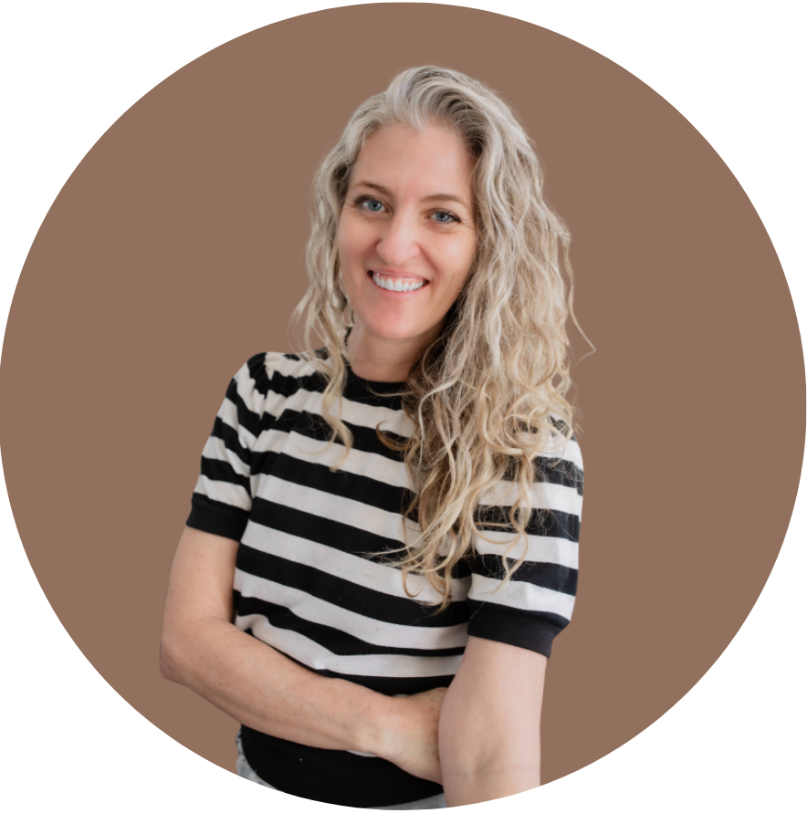 A woman with long, curly blonde hair smiles and crosses her arms, wearing a black and white striped shirt against a plain brown background.