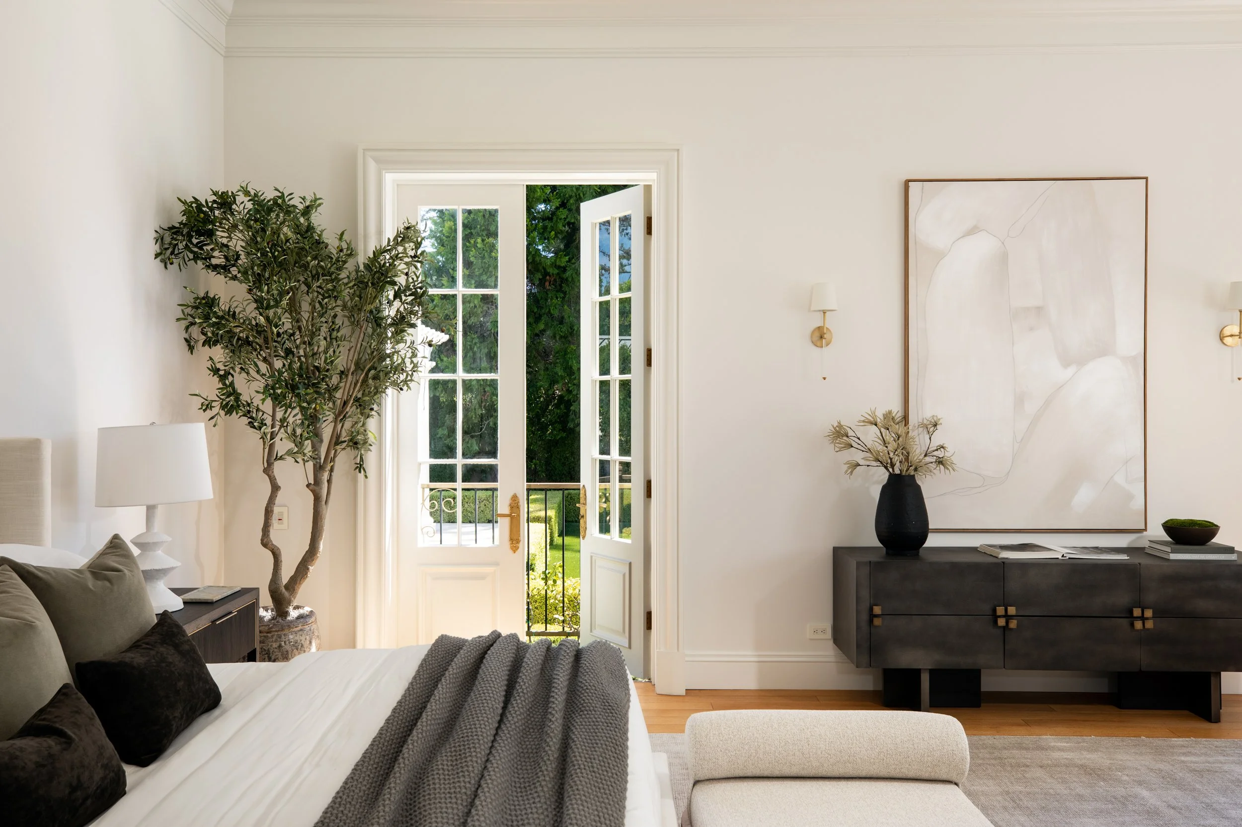 Living room with large glass door leading outside, decorated with a tall potted plant, a white lampshade, and modern art on the wall.
