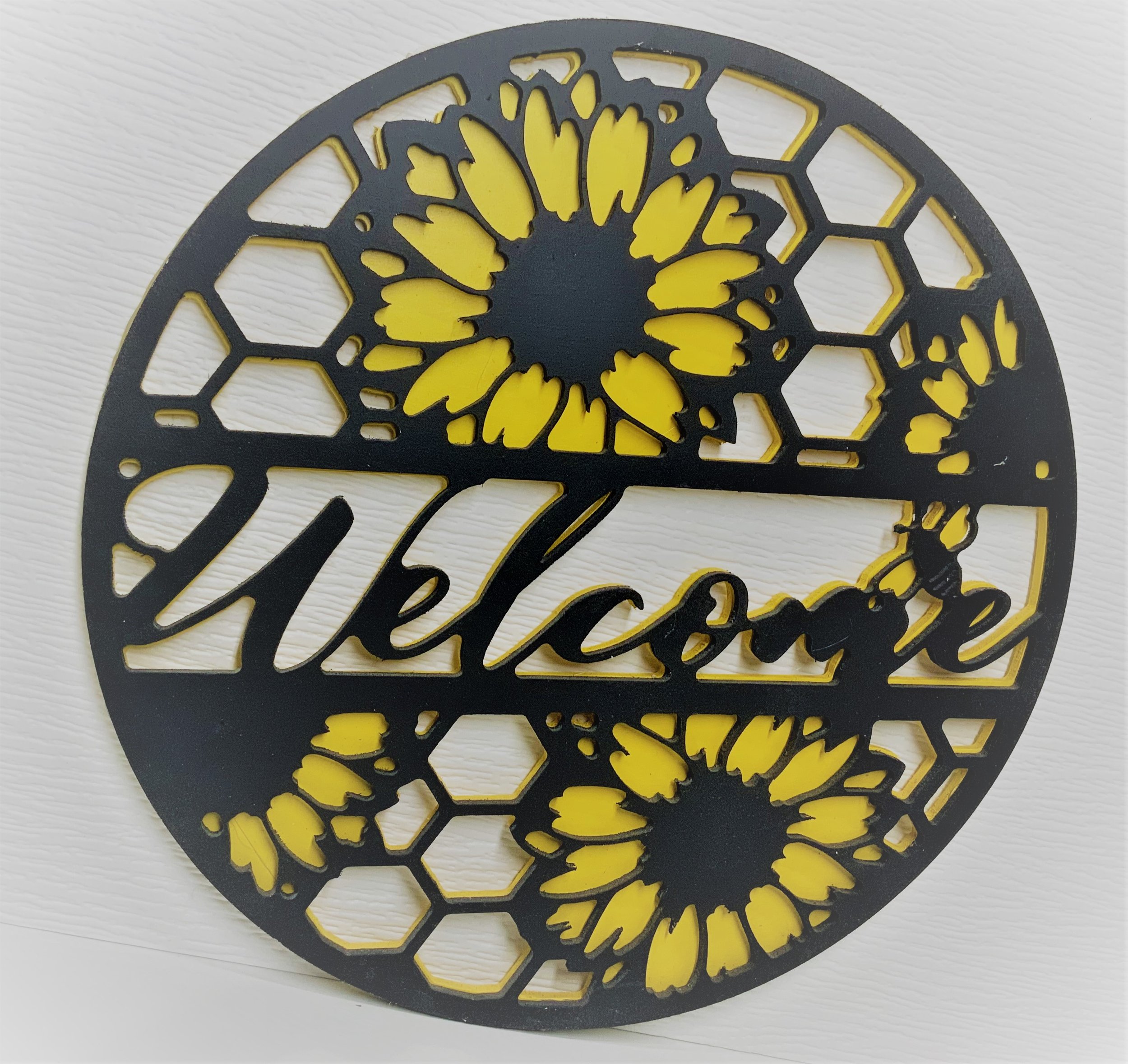 Close-up of a decorative circular metal piece with a black outline and yellow sections, featuring a floral or organic design, placed on a white textured surface.
