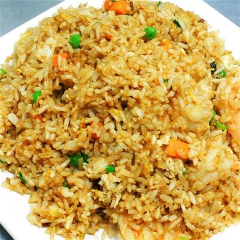 Close-up of a plate of fried rice with vegetables such as peas and diced carrots.
