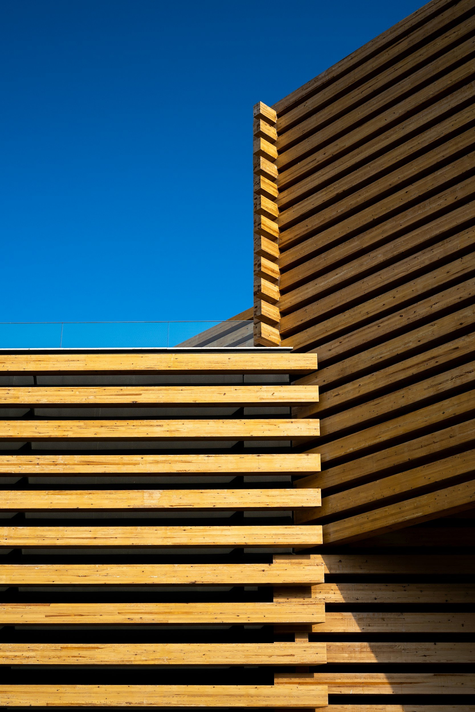 Close-up of a modern building with horizontal wooden slats on the facade, against a clear blue sky.