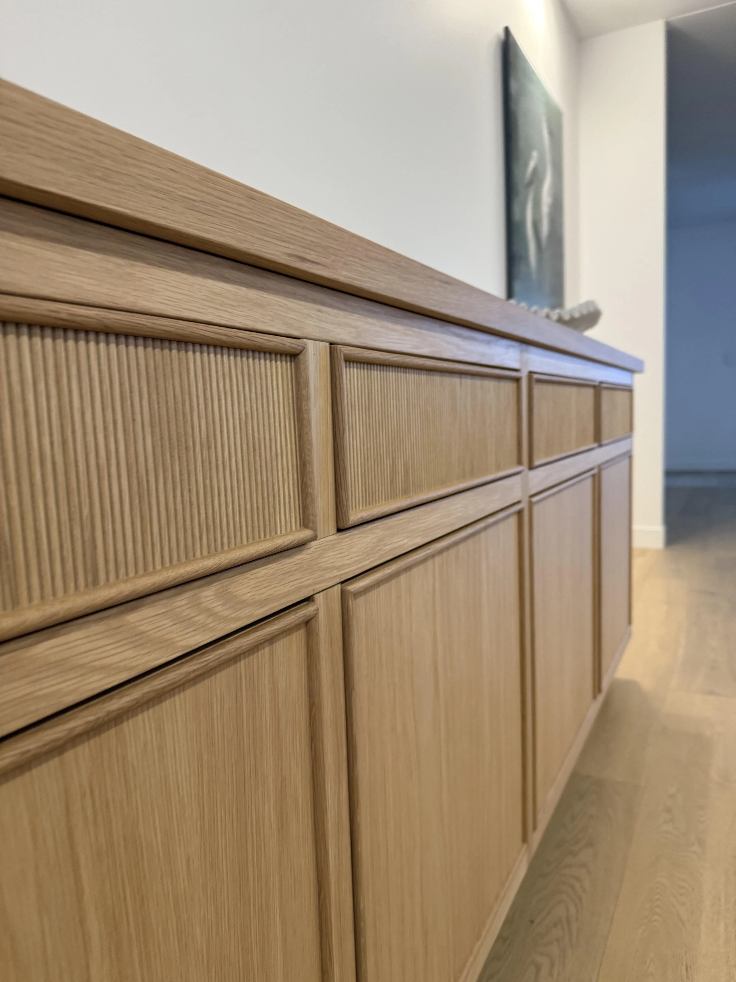 Close-up of a wooden cabinet with carved pattern doors, placed in a room with a light-colored wall and wooden flooring.