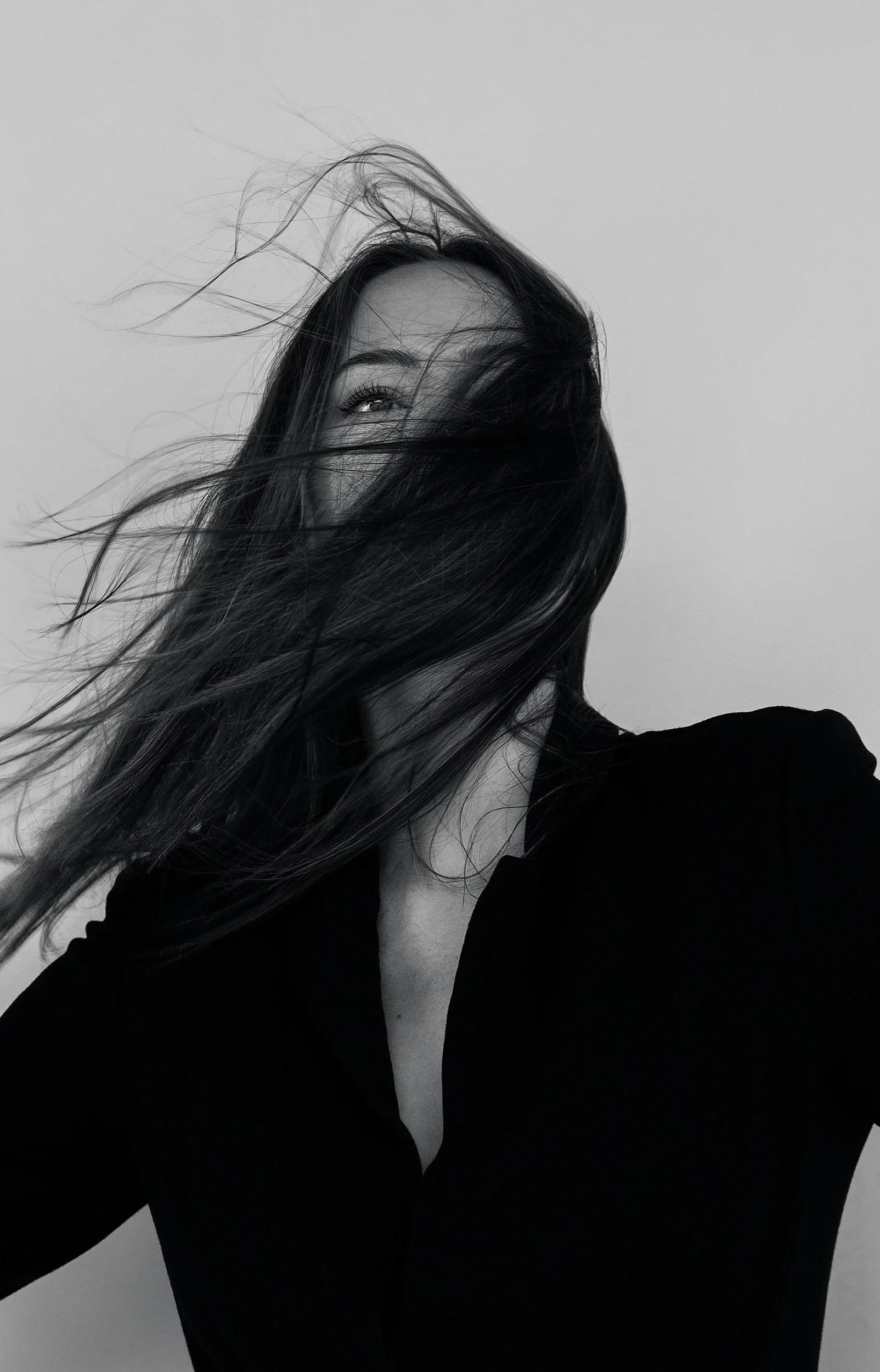 Black and white photo of a woman with long hair, partially obscuring her face, wearing a black top with a deep neckline.