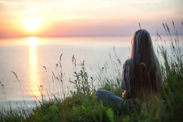 a woman sitting looking at the sunset over the ocean